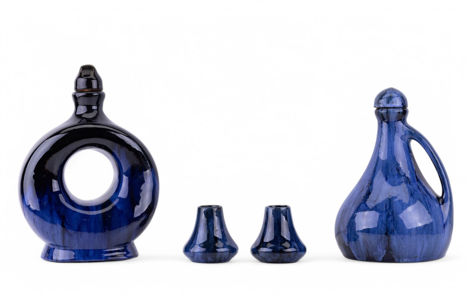 Cobalt Blue McCoy Bottles and Candle Holders: Cobalt blue McCoy doughnut shape bottle with cork stopper measuring approx. 11.25" H x 8" W x 4.5" D, handled jug with music box at the base, and 2 matching candle holders approx. 3" H.