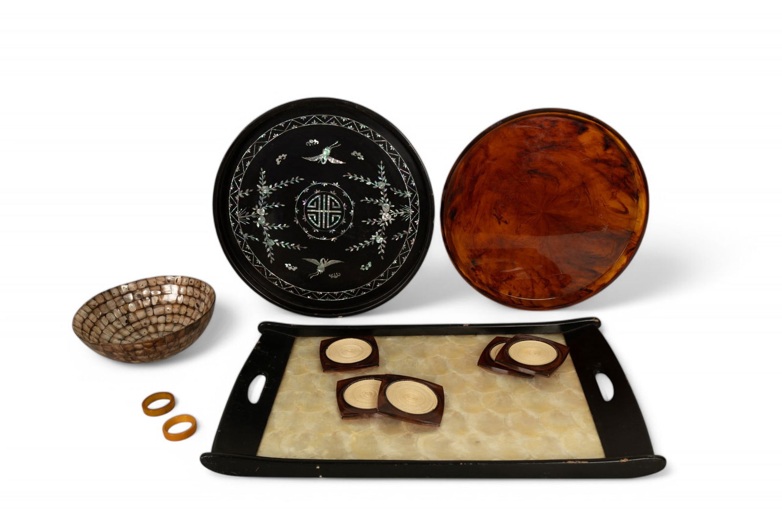 Mid Century and MoP Decorative Trays and Coasters: Group of items including three decorative serving trays and five coasters. The first tray showcases a faux tortoiseshell Lucite, 14". The second, a round black tray, features an intricate inlaid mothe