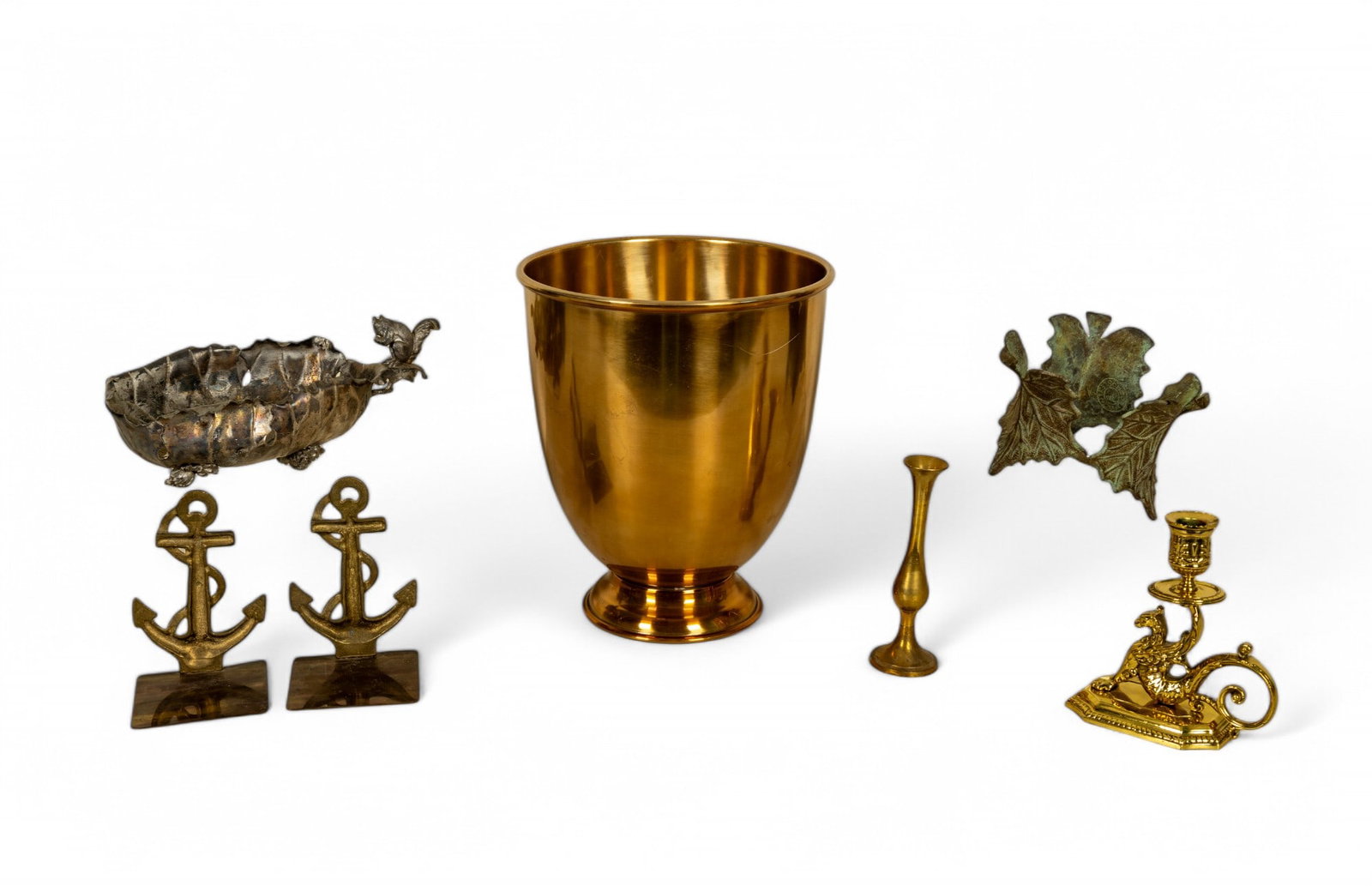 Mixed Metal Decorative Pieces: Assorted decorative items made of brass and other metals. Includes a large polished metal jardiniere, a pair of anchor-shaped brass bookends, a small brass bud vase, an ornate dragon-style brass candl