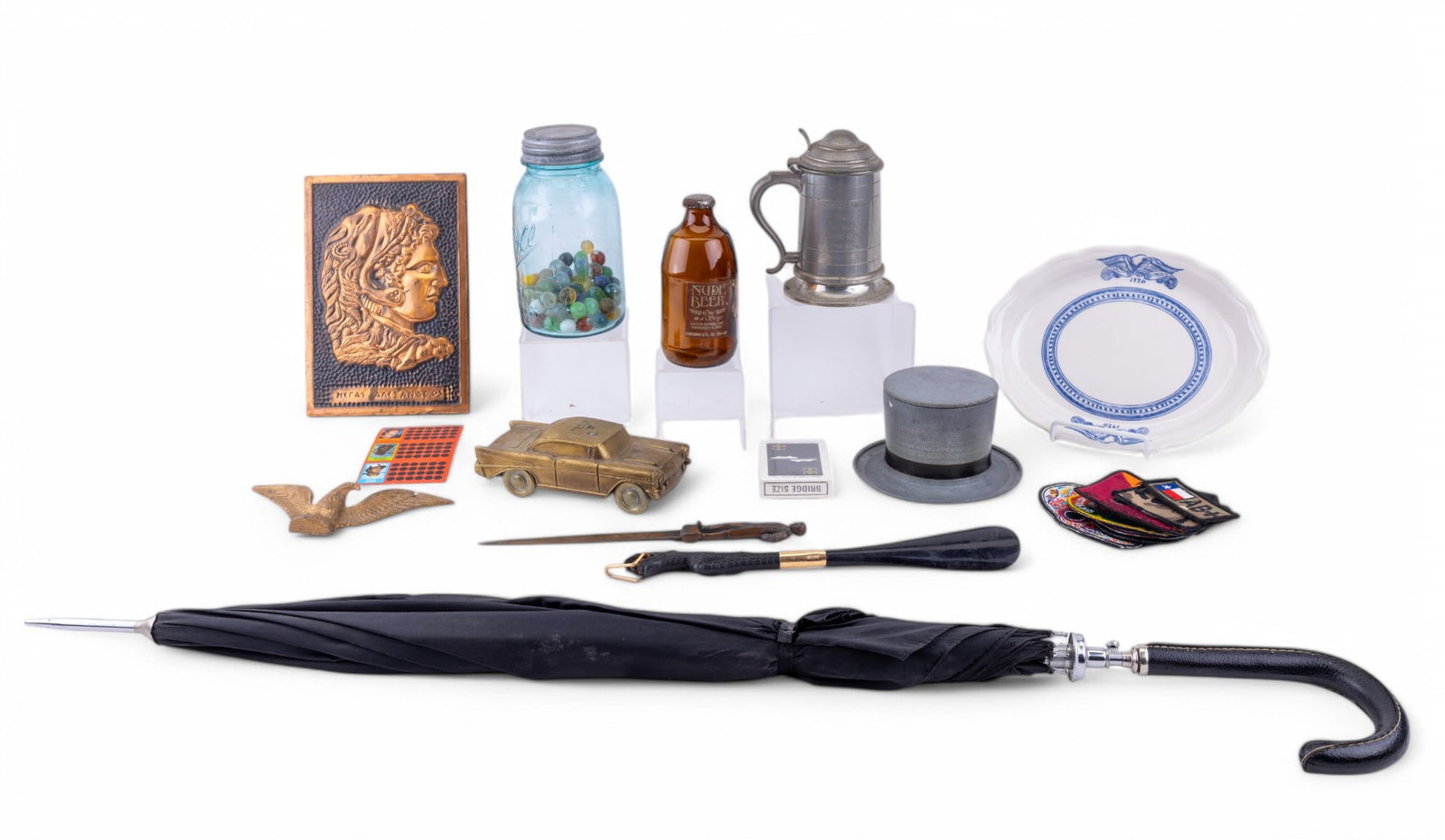Men's Grooming and Mantiques: A diverse lot of collectibles comprising items such as a metallic top hat shaving cream container, a black umbrella with a curving handle, a bronze decorative car bank, patches with various designs, a