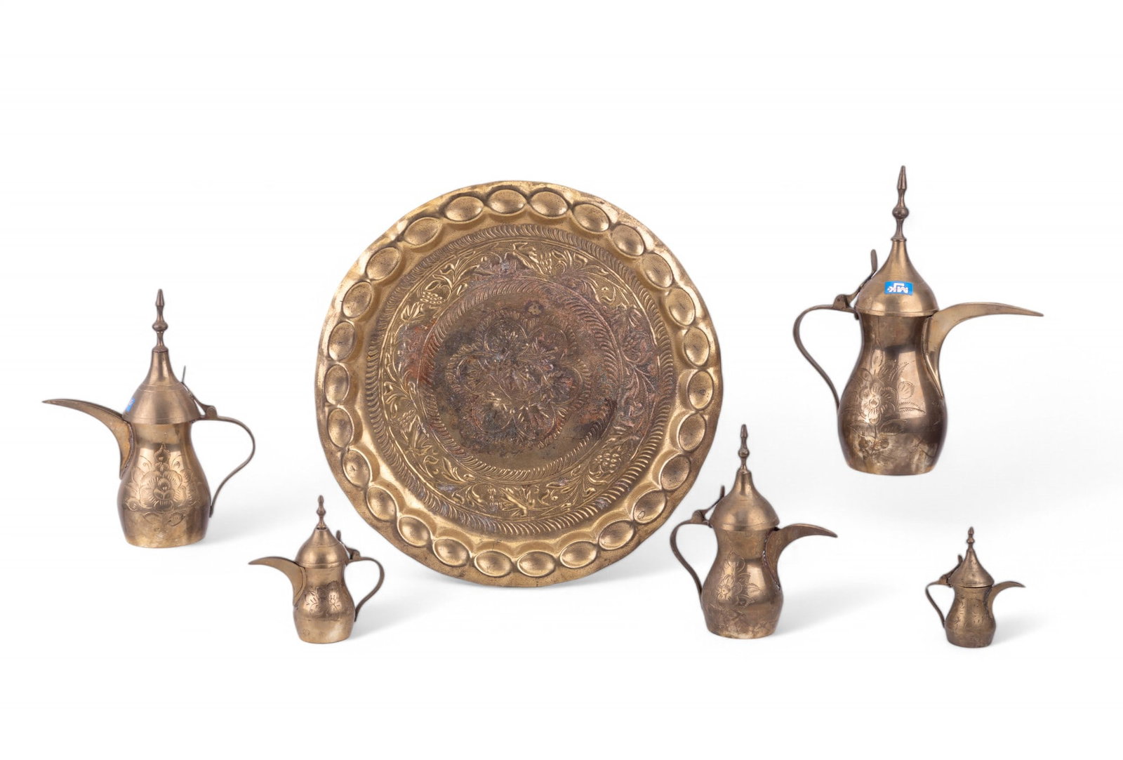 Brass Charger w/ 5 Arabic Dallah Coffee Pots: Brass charger with floral stamped motifs and scalloped rim measuring 15.5" Dia.; has some wear and oxidation. 5 brass Arabic Dallah coffee pots ranging from 4" H to 11" H.