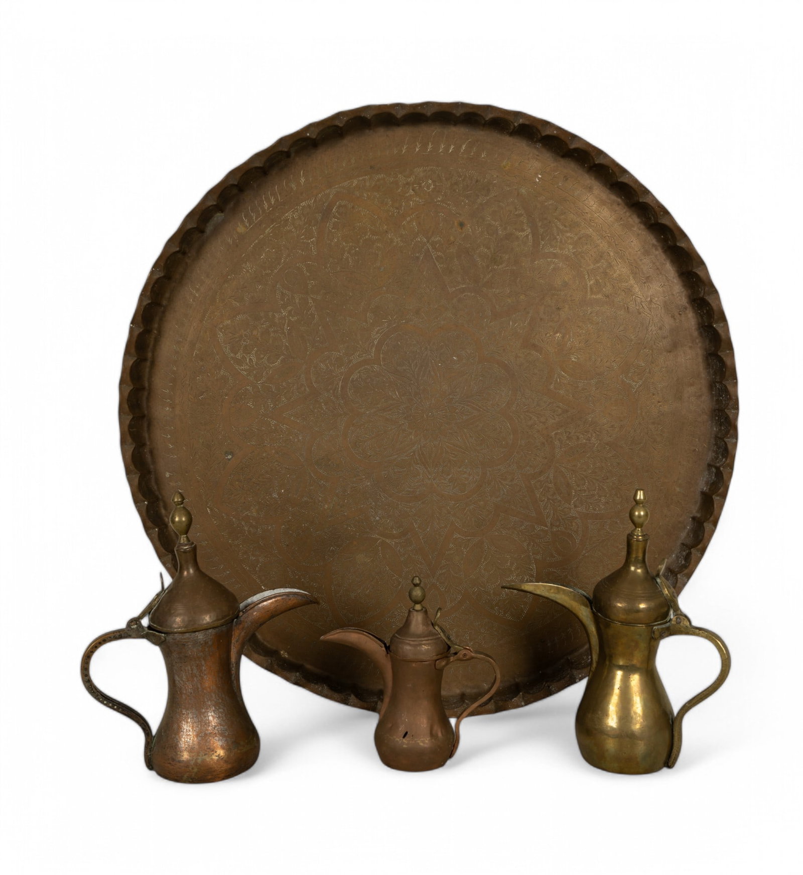 Large Brass Charger w/ Arabic Dallah Coffee Pots: Large brass charger with engraved floral designs and a scalloped rim measuring approx. 33.5" Dia. x 2" H. 3 brass and copper Arabic Dallah coffee pots ranging from 9.5" H to 13.5" H.