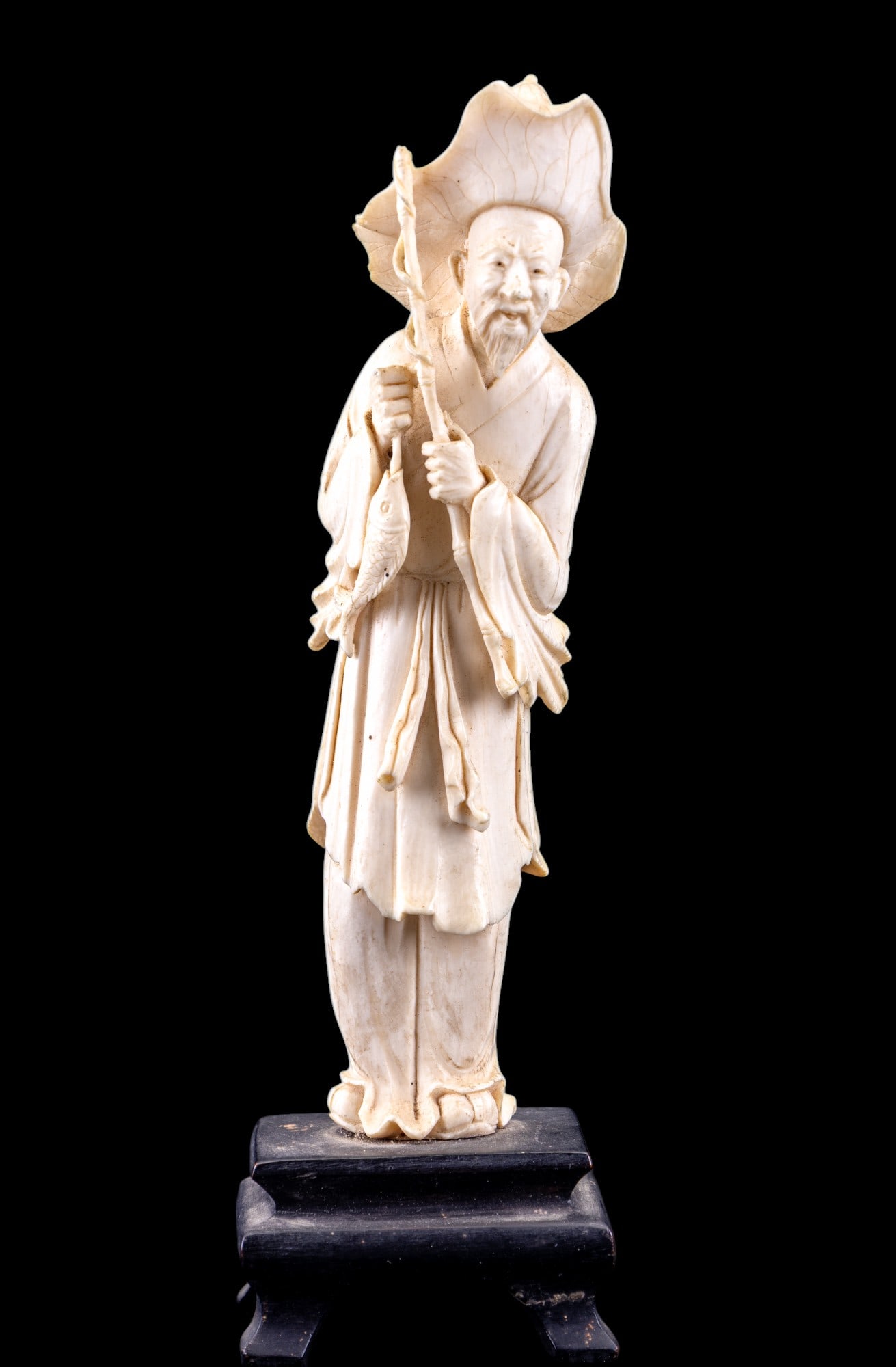 Chinese Carved Bone Fisherman Figurine on Stand: Chinese carved bone / natural figurine of a fisherman on a wooden stand. Fisherman features a large hat, a fishing rod in his left hand (broken piece at top), & a fish in his right hand. Figurine meas
