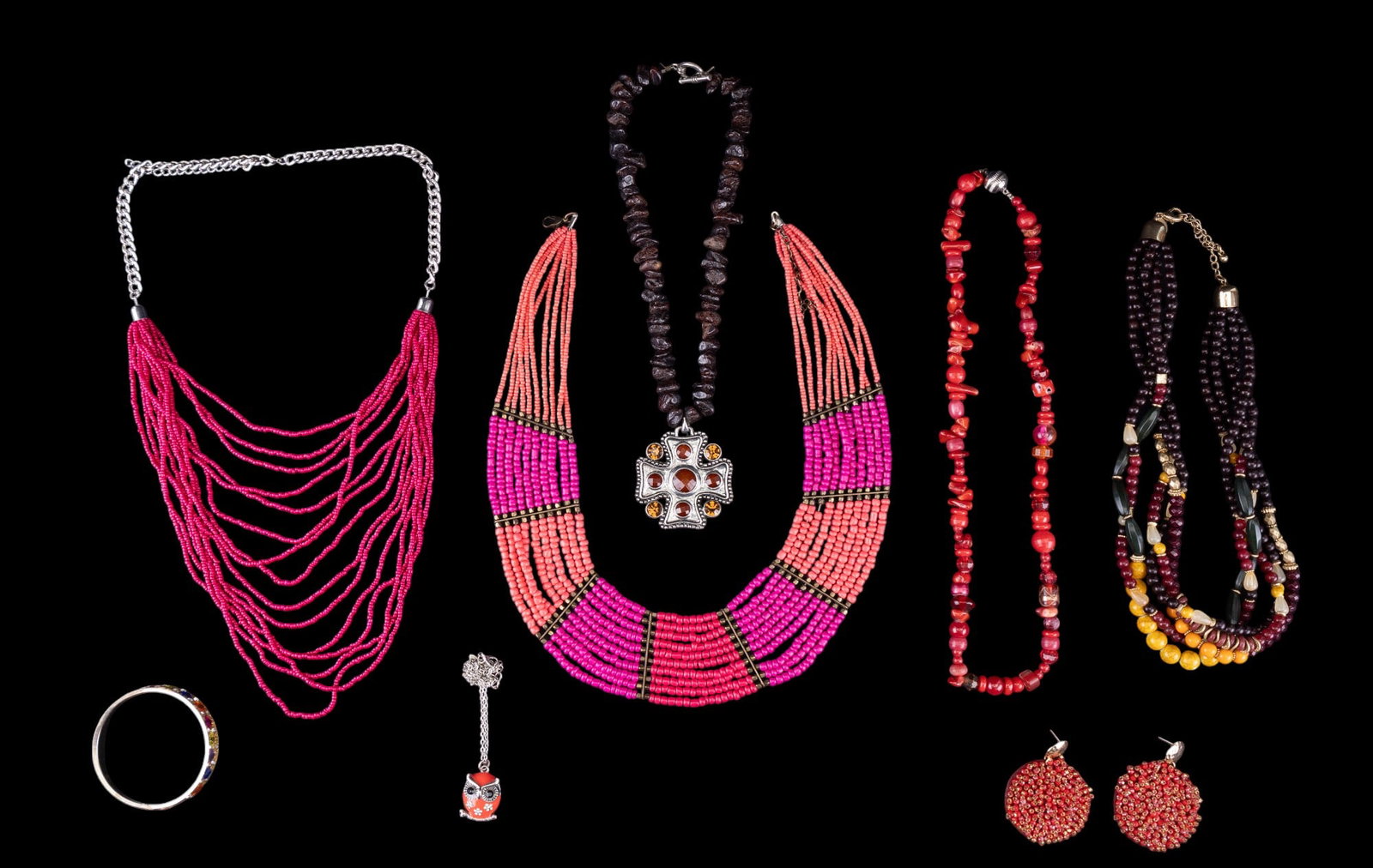 Red and Pink Stone and Bead Necklaces: Toggle clasp necklace with strand of natural garnets and silver tone cross pendant, multistrand pink microbead necklace, enamel owl pendant, silver tone and multicolor rhinestone bangle, and more.