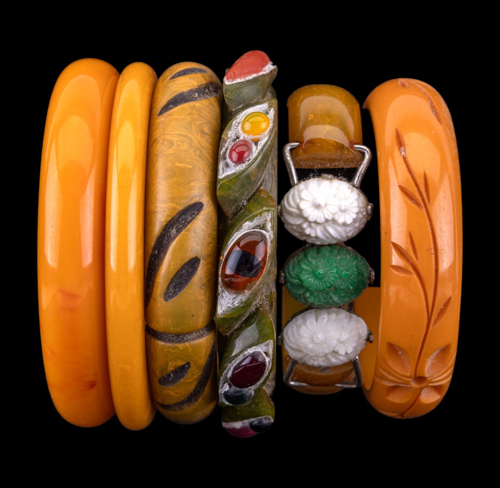 Vintage Bakelite Bracelets: Three carved Bakelite bangle bracelets, two orange bangles, and Bakelite bangle with hinged floral detail.