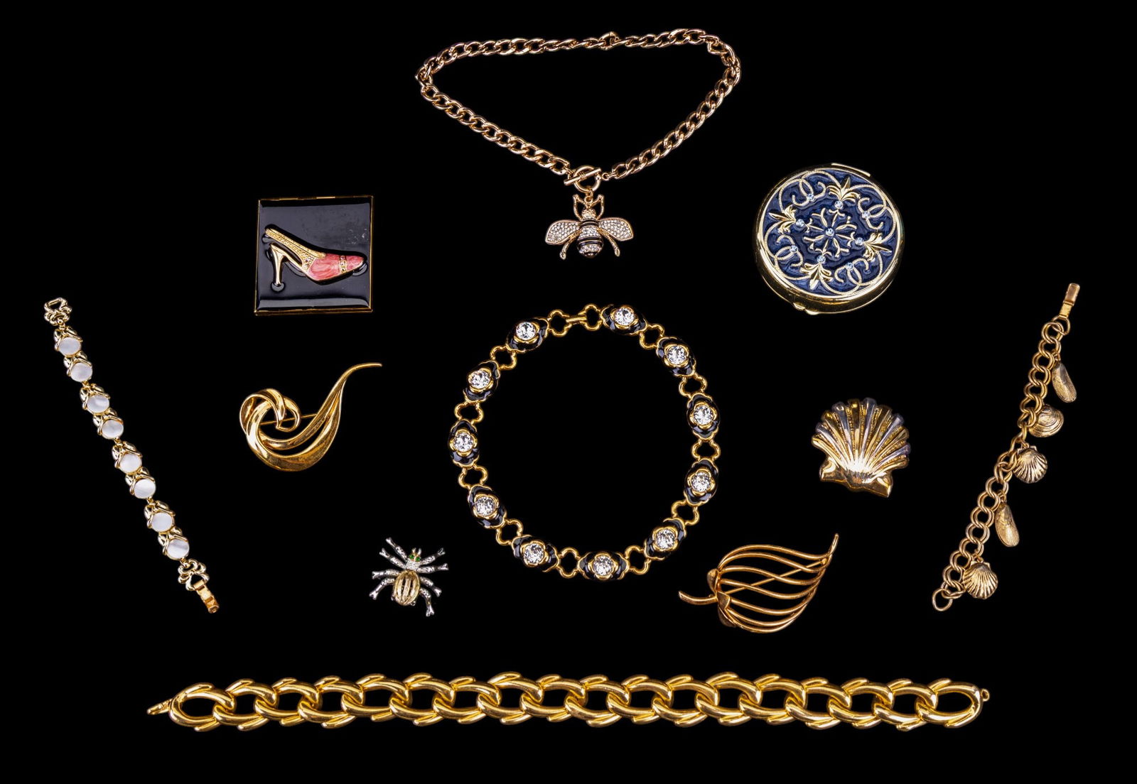 Monet, Napier, + More Gold Tone Jewelry (11 Pcs.): Collection of 11 gold tone jewelry pieces including a Monet chain link necklace w/ black enamel + clear rhinestones, a Napier strawberry brooch, an Avon flowy leaf brooch, a Best seashell brooch, a br