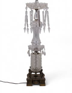 Tall Crystal and Brass Table Lamp W/ Prisms: A vintage cut crystal table lamp with ornate brass base featuring mythological figures at each corner. The multi-tiered body includes deeply faceted glass elements and a scalloped glass dish top adorn
