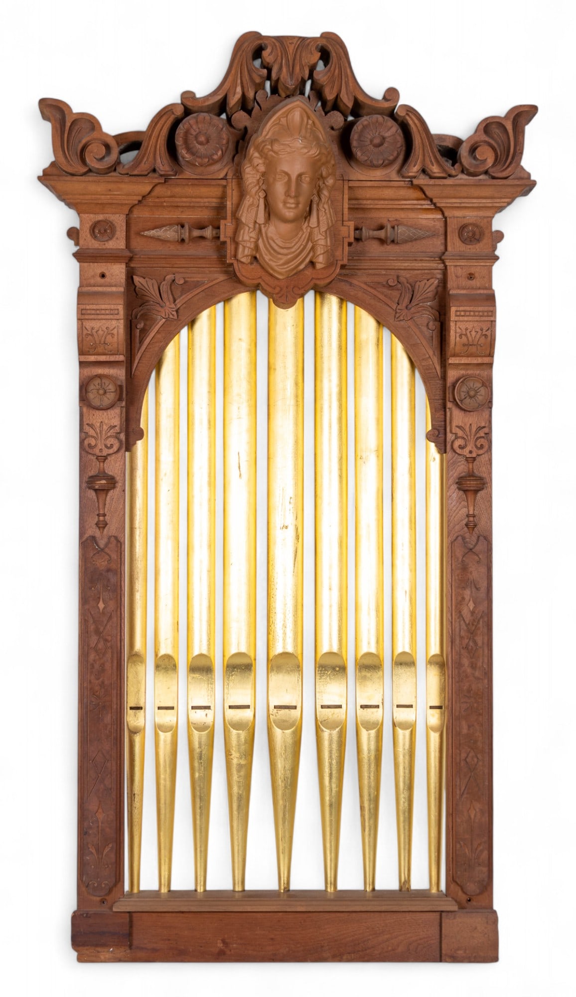 Carved Walnut Arched Panel: A carved walnut panel Gothic arch shape, featuring a central terracotta face with surrounding foliate and floral motifs. The lower section is a series of gilt painted carved faux organ pipes. Has a ho