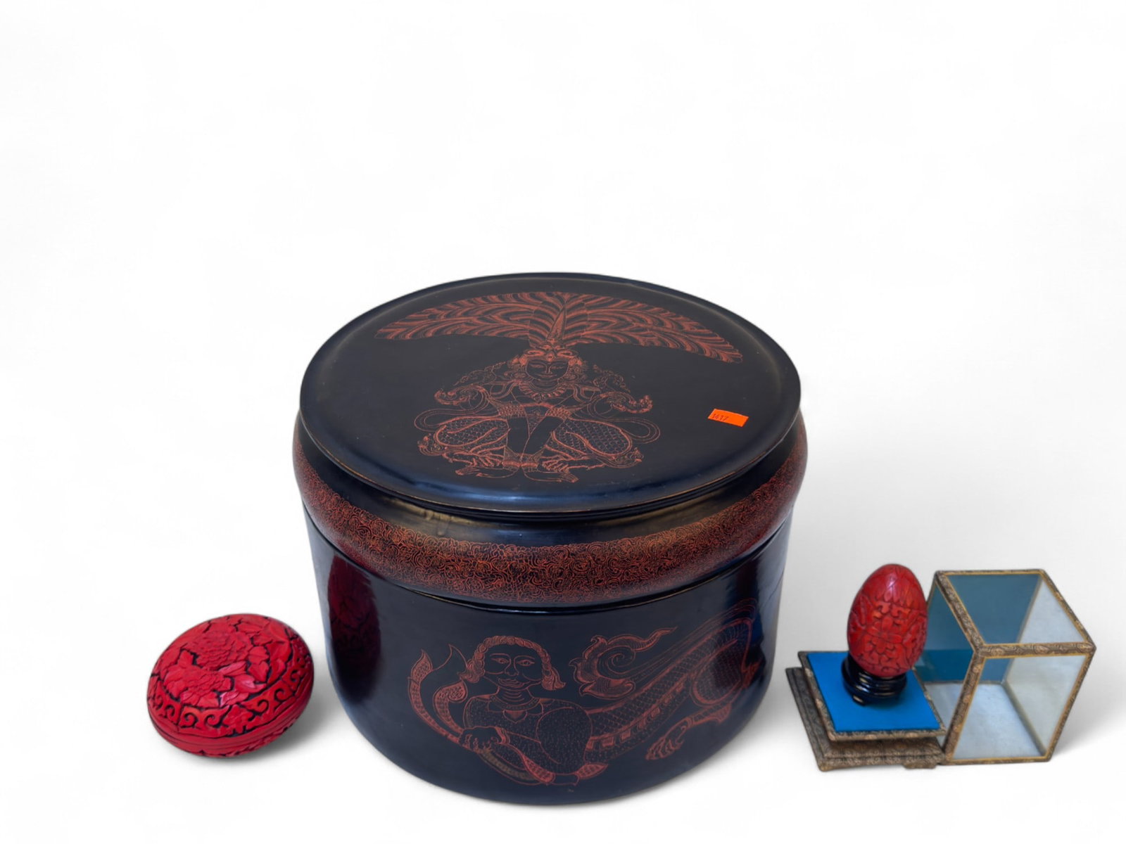 Asian Lacquerware Items: A large Asian lacquered storage box with a domed lid, decorated in red on black with Buddhist-style designs. Sides feature mythological figures with serpent-like bodies, and the lid shows a seated fig