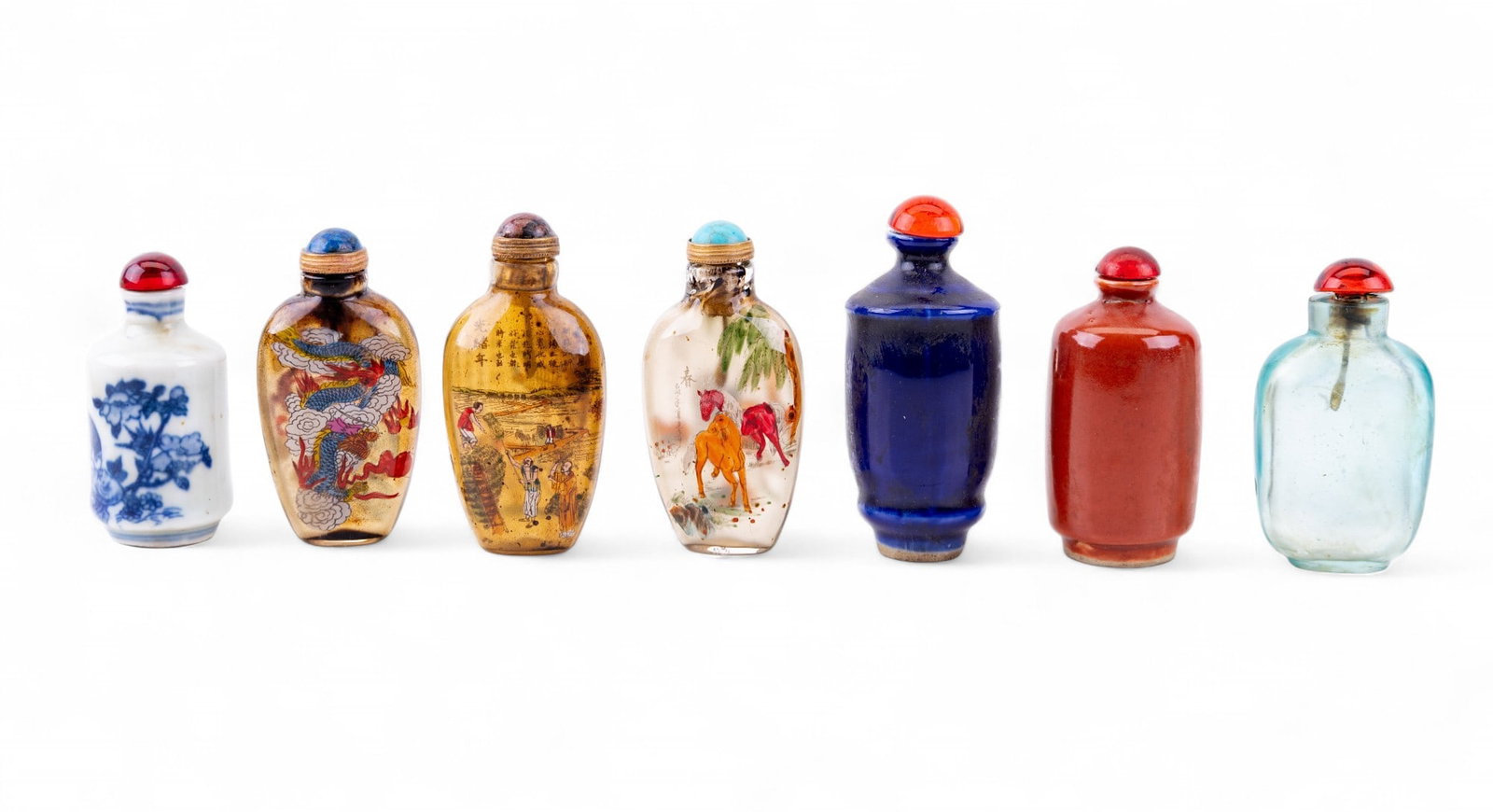 Glass and Porcelain Snuff Bottles: A collection of seven Chinese snuff bottles including designs such as clear aqua blue glass, blue on white porcelain, solid dark blue and burnt orange porcelain, and three clear reverse painted glass