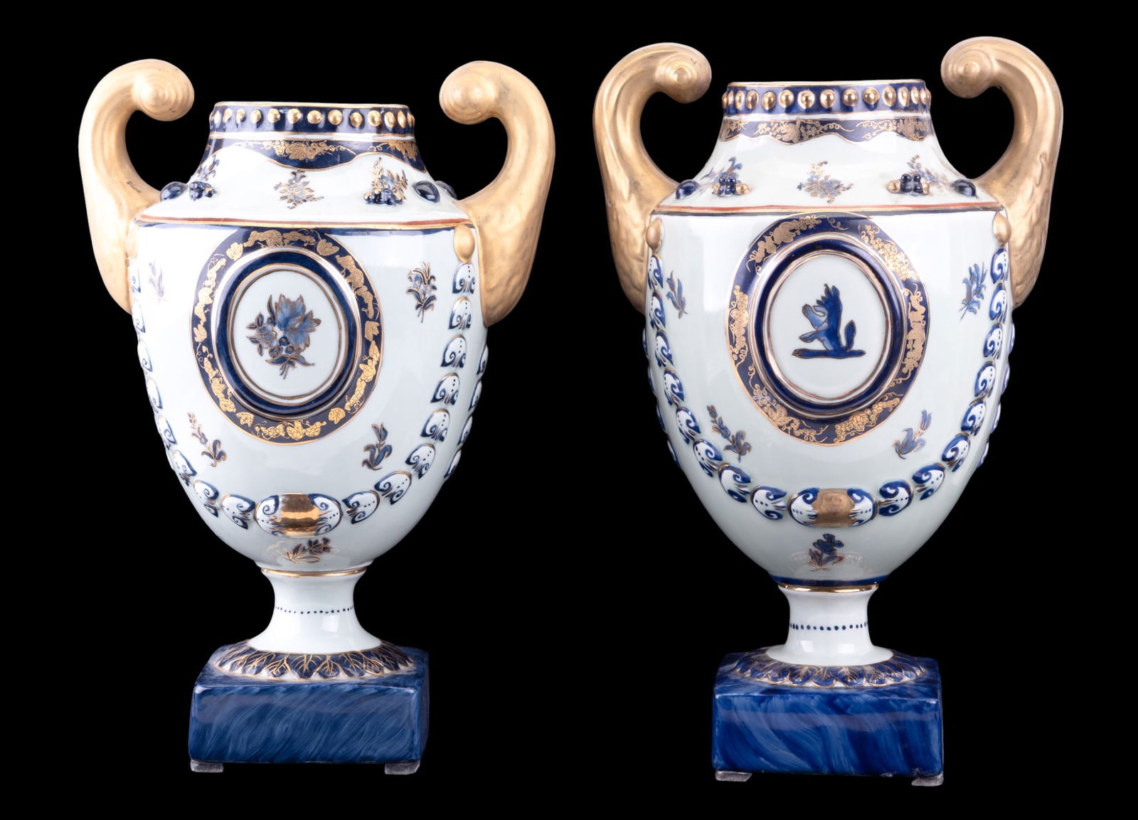 Pair of Chelsea House Porcelain Urns with Lids: Pair of porcelain urns with lids by Chelsea House, decorated in gilt and cobalt blue in neoclassical style, each featuring medallion moitfs and scrolled gilt handles. Marked "Chelsea House". Each meas