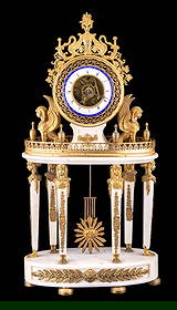 French Egyptian Revival Marble Mantle Clock: French white marble mantel clock decorated with gilt bronze mounts in the Egyptian Revival Style. Clock is supported on 6 marble columns with figural busts. Each side of drum case is flanked by winged