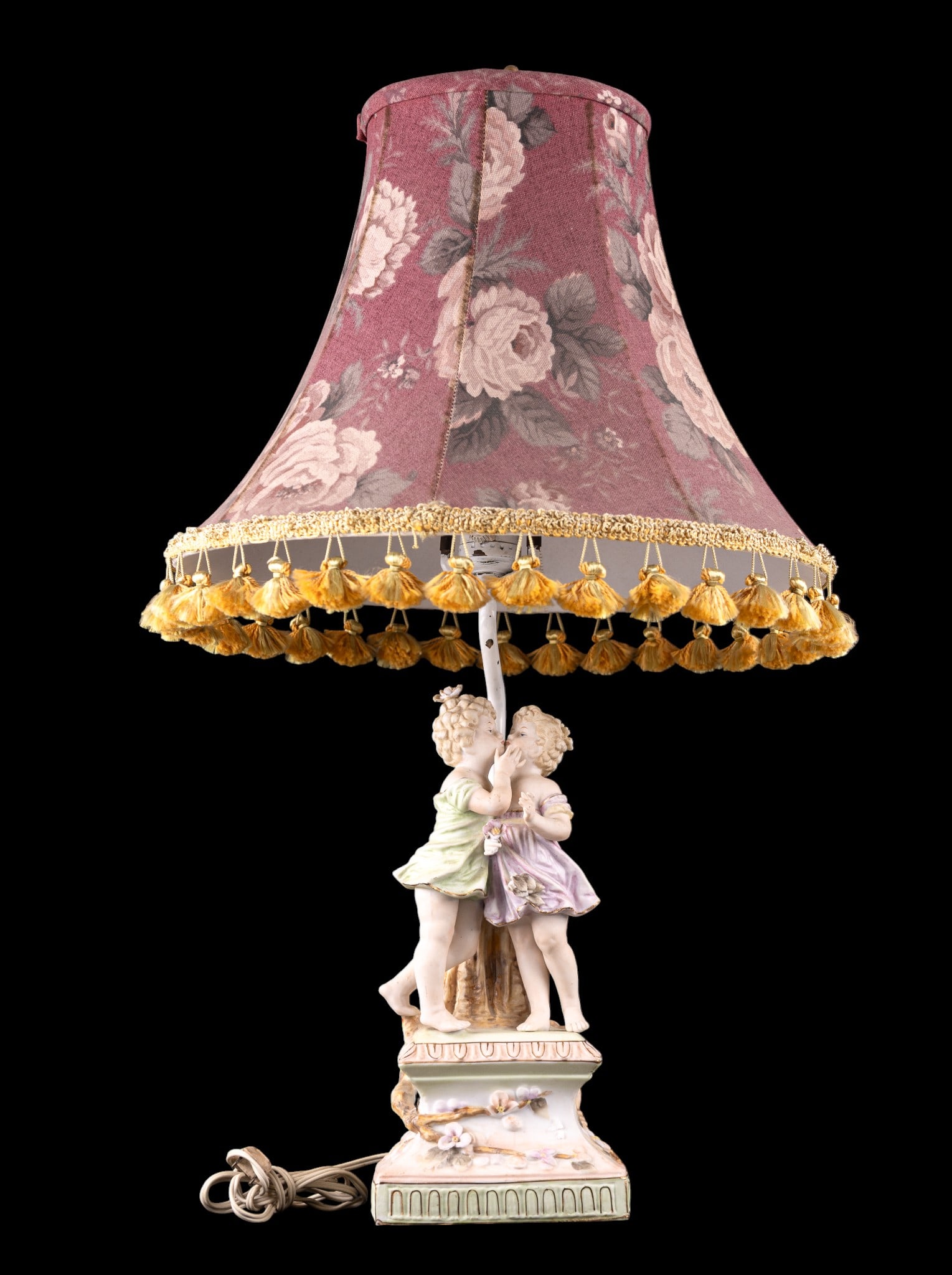 Bisque Porcelain Figural Lamp: A vintage bisque porcelain figural table lamp depicting two little girl son a floral base, featuring a floral linen shade with golden tassels, untested, measures approx. 25" H to the finial. Note some