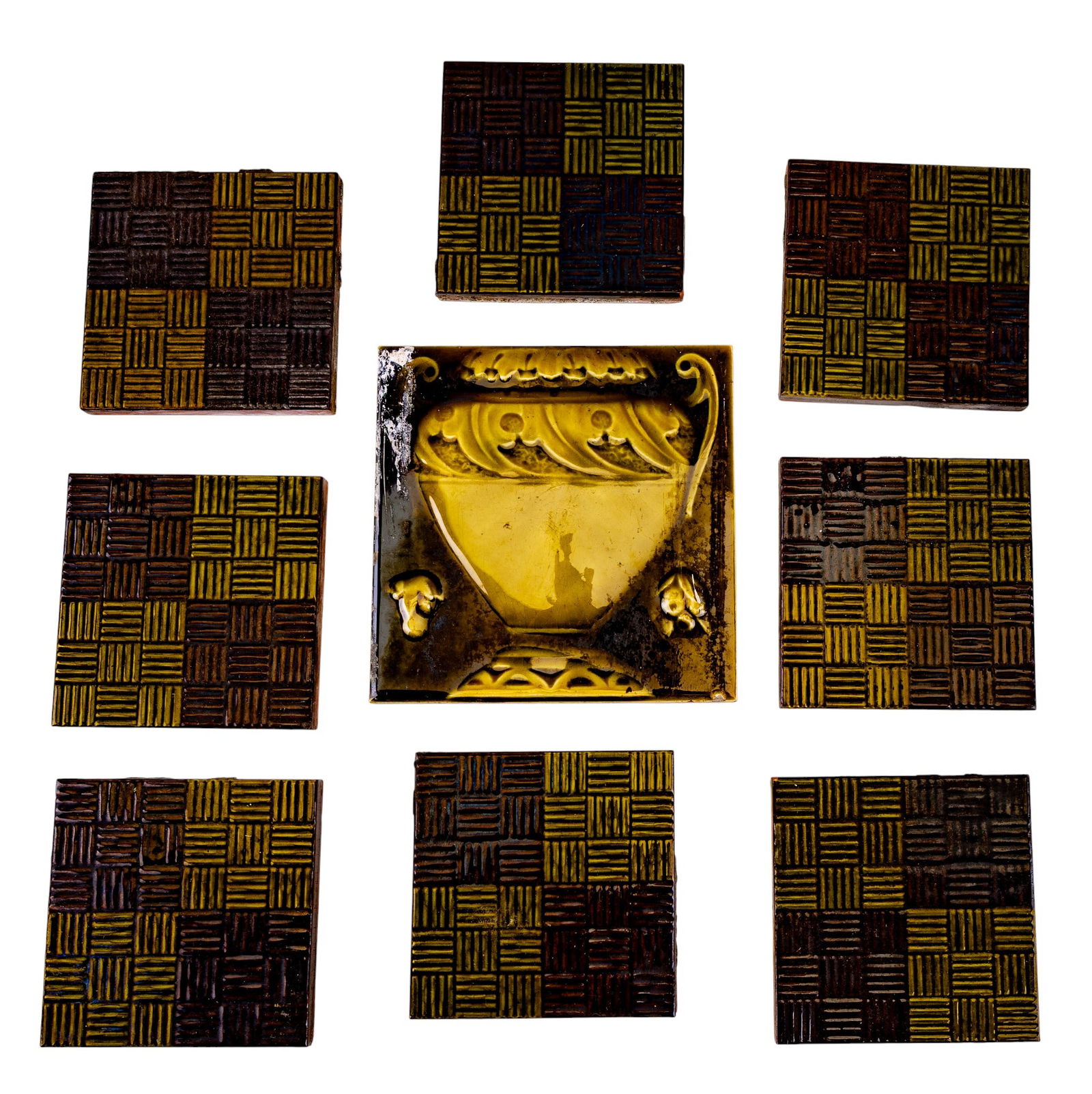 9 Vintage Glazed Ceramic Tiles: 9 vintage glazed ceramic tiles including 8 checkerboard-pattern tiles in mustard yellow and brown, together with one larger relief tile depicting a classical urn. Largest tile measures approx. 6" squa