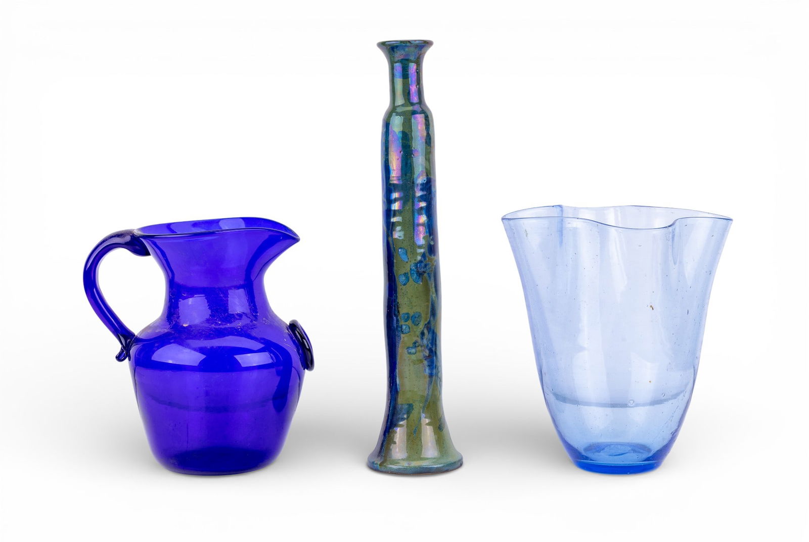 3-Piece Hand-Blown Art Glass: 3 hand-blown art glass pieces, including a cobalt pitcher with applied pineapple motif, a tall slender bud vase with variegated green and blue glaze, and a light blue free-form vase. Bud vase measures