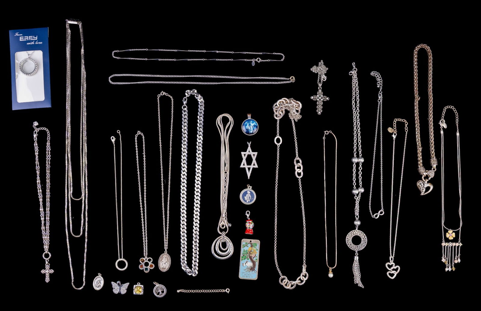 Silver Tone Charms, Chains, and Pendants: A collection of silver tone jewelry featuring a Cuban chain, Brighton heart shaped lock and Cross pendant necklaces, enamel gum ball machine charm, Star of David pendant, Catholic prayer medallions, a