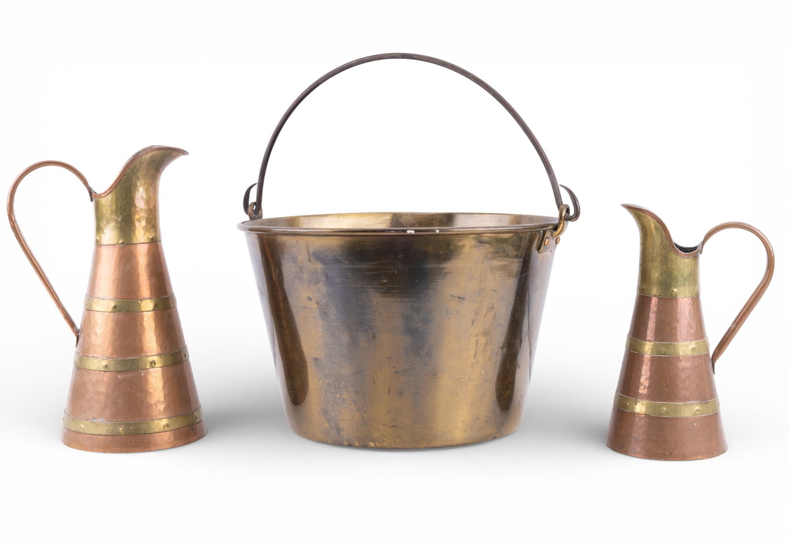 Hammered Brass Bucket, Copper Pitchers: Lot includes 1 hammered brass bucket with swing handle and rolled rim, along with 2 hammered copper pitchers of graduated size. Bucket measures approx. 8.5" H x 12.5" diameter. Larger pitcher measures