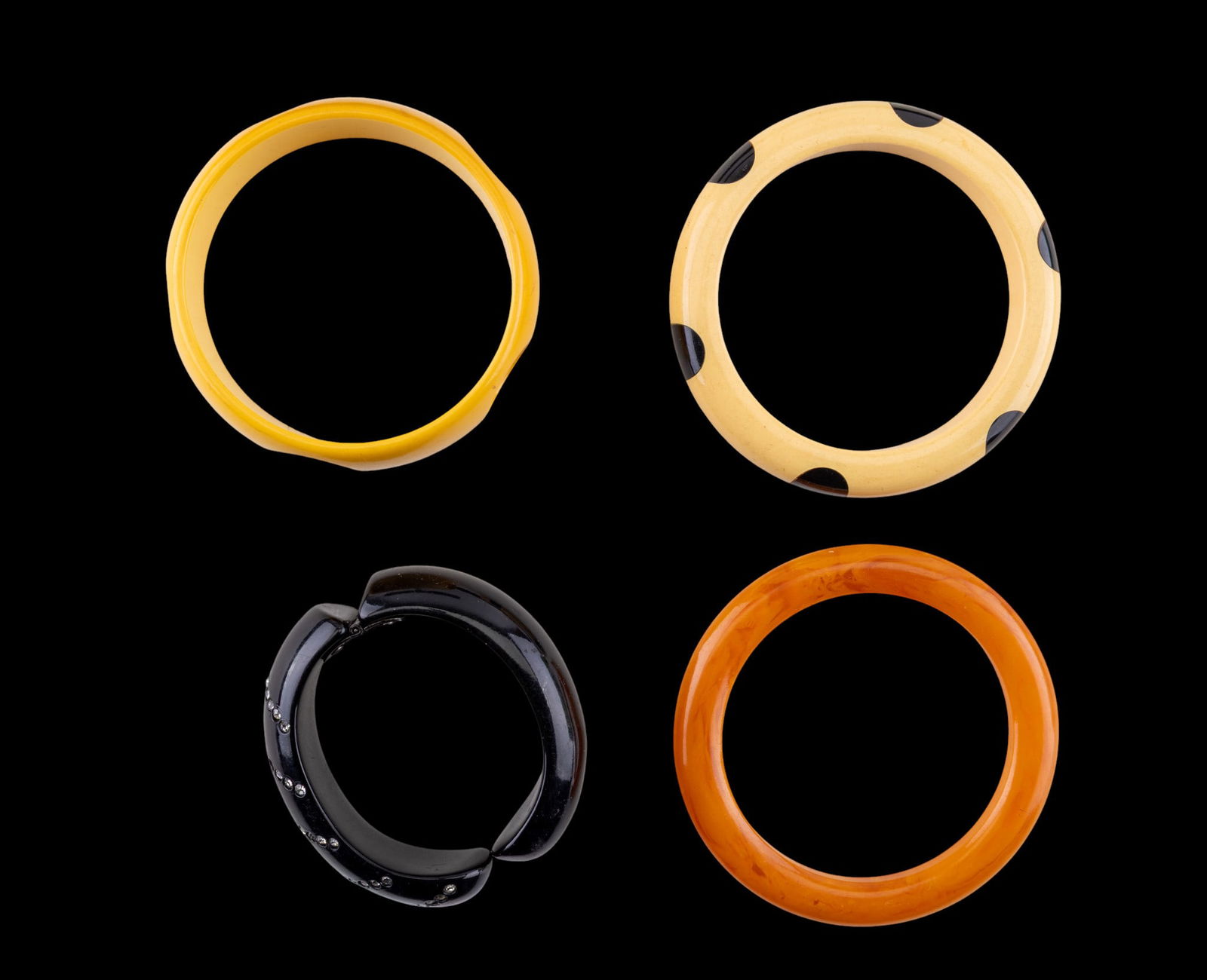 Bakelite and Other Bracelets: 4 bangle bracelets with a tan and black dot bakelite bracelet, an orange and a pale yellow bracelets and a black lucite and rhinestone hinged cuff bracelet.
