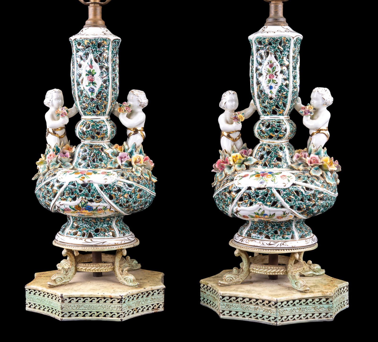 Early Italian Reticulated Porcelain Lamp Pair: A pair of matching early Italian reticulated porcelain lamps featuring gilt cherubs and flowers and painted metal bases with dolphin feet, marked 'ITALY' on the under side of the porcelain section, un