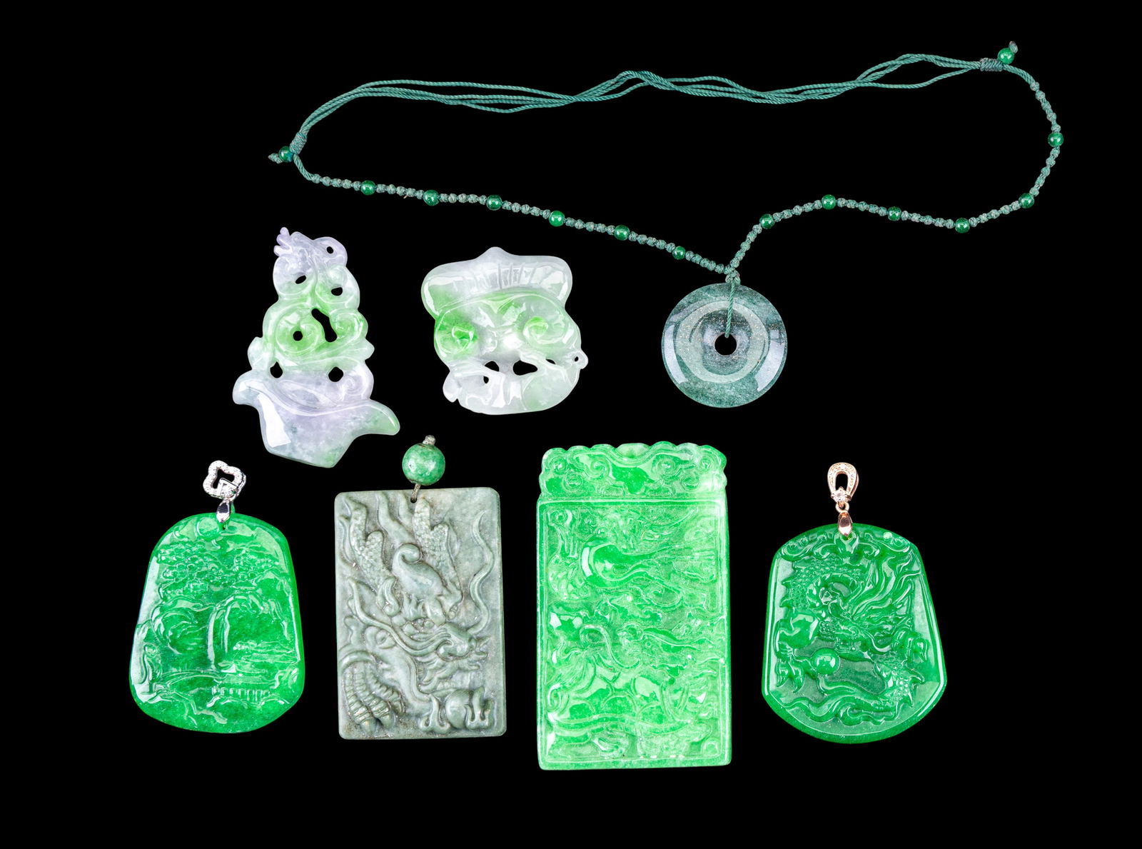 Jade Dragon Medallions: A collection of jade medallions including two white, green, and purple jade dragon and foo dog medallions, an apple green jade pendant with silver tone bail depicting a village scene, two apple green