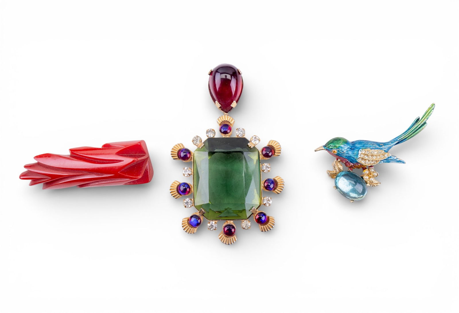 Bakelite and Other Vintage Brooches: A vintage enamel bird brooch with pale blue cabochon, a gold tone brooch with a large green facet cut rhinestone and red cabochon, and a carved red Bakelite brooch.