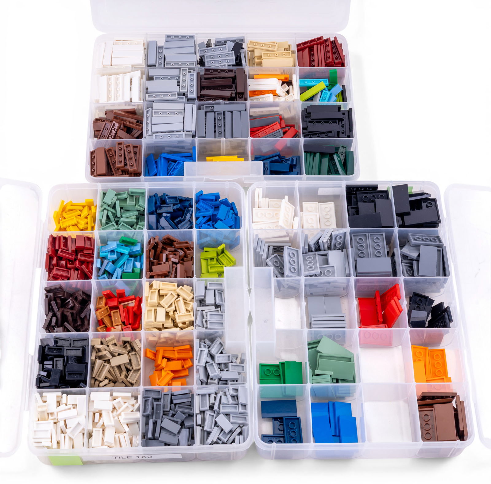 Lego Tile Pieces in Assorted Sizes and Colors: LEGO tile pieces organized in labeled storage boxes. Includes 2x4, 1x4, and 1x2 tile dimensions in a variety of colors such as white, black, gray, red, green, blue, and beige. Items are neatly sorted