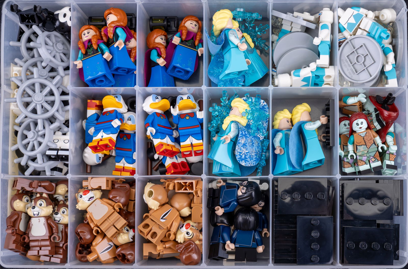 Container of Disney LEGO Series 2 Extras: Plastic storage container with multiple compartments holding LEGO minifigure parts and accessories from Disney LEGO Series 2. Contents include fully assembled and spare parts, such as characters and t
