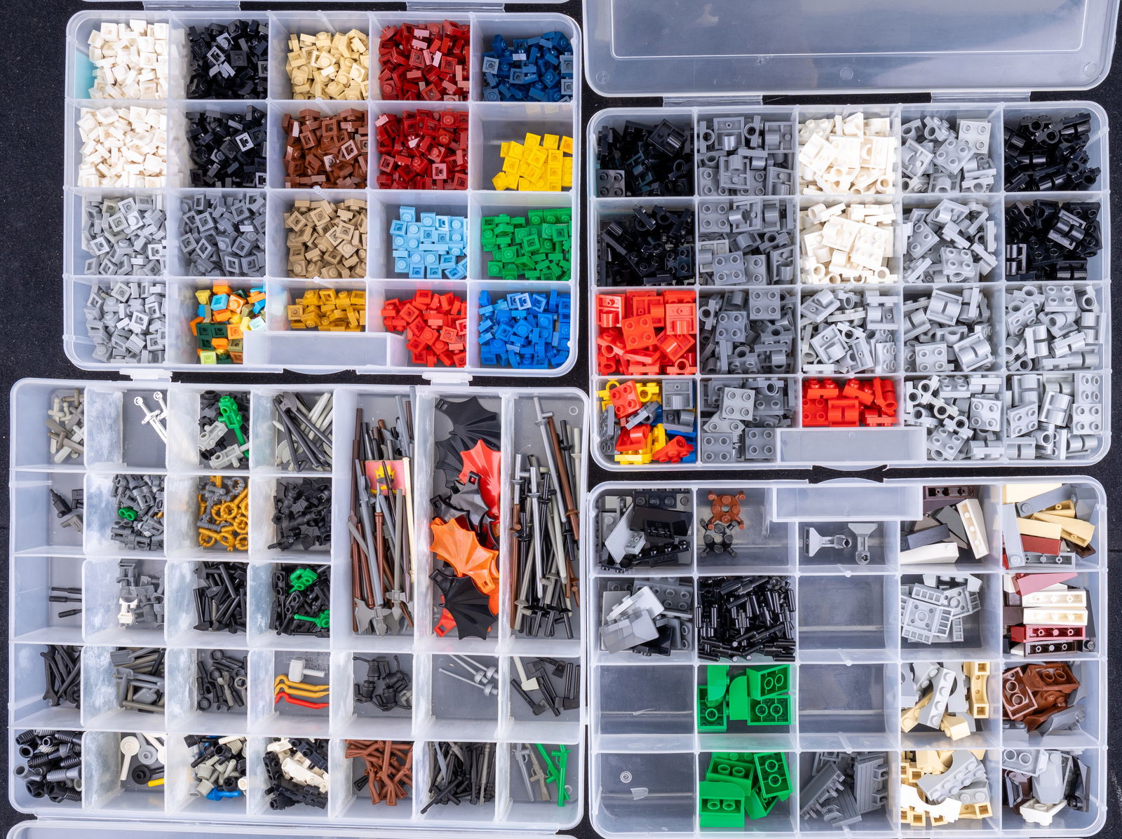 LEGO Pieces in Storage Containers: LEGO pieces organized in compartmentalized plastic storage containers. Includes plates, modified plates, and various specialized parts in a range of colors such as gray, black, red, and green. Compart