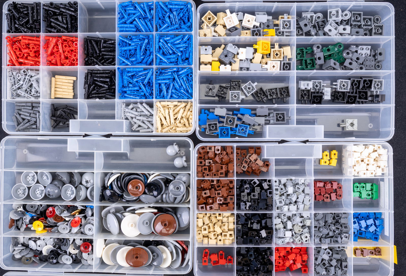 Four Containers of Assorted Lego Pieces: Four plastic storage containers organizing assorted Lego pieces by type and color. Includes Technic long pins, modified bricks (1?1 and 2?2), and hemisphere-shaped dish pieces ranging from 2?2 to 4?4.
