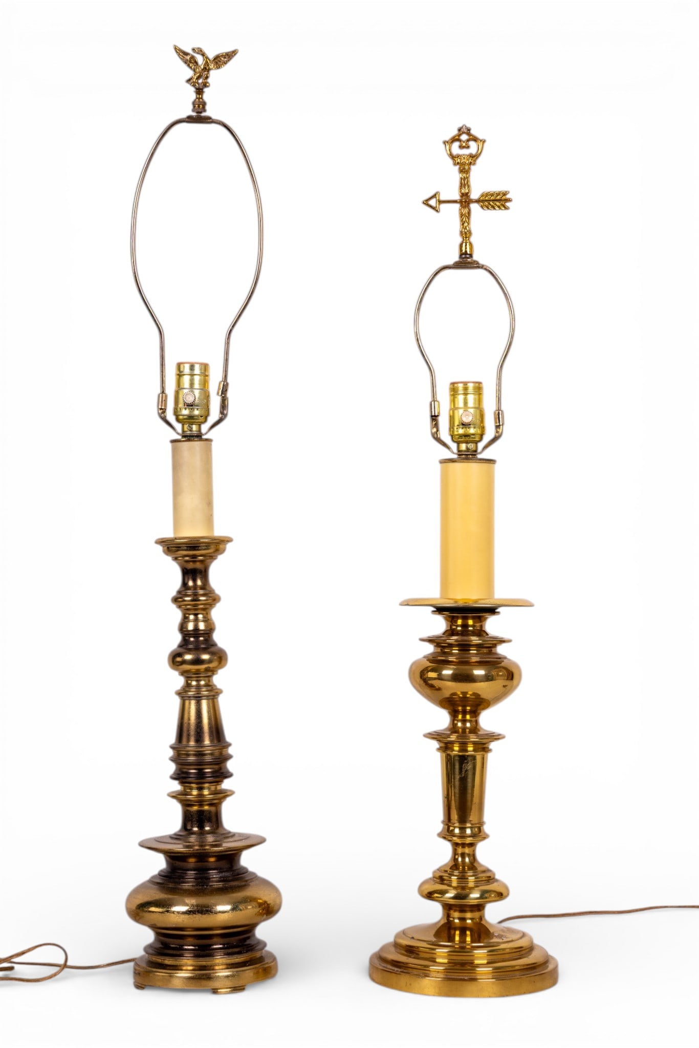 Brass Table Lamps with Ornate Finials: Brass table lamps featuring sturdy pedestal bases and detailed finials. One finial depicts an eagle with wings spread, while the other features an intricate arrow design. Lamps include harp frames