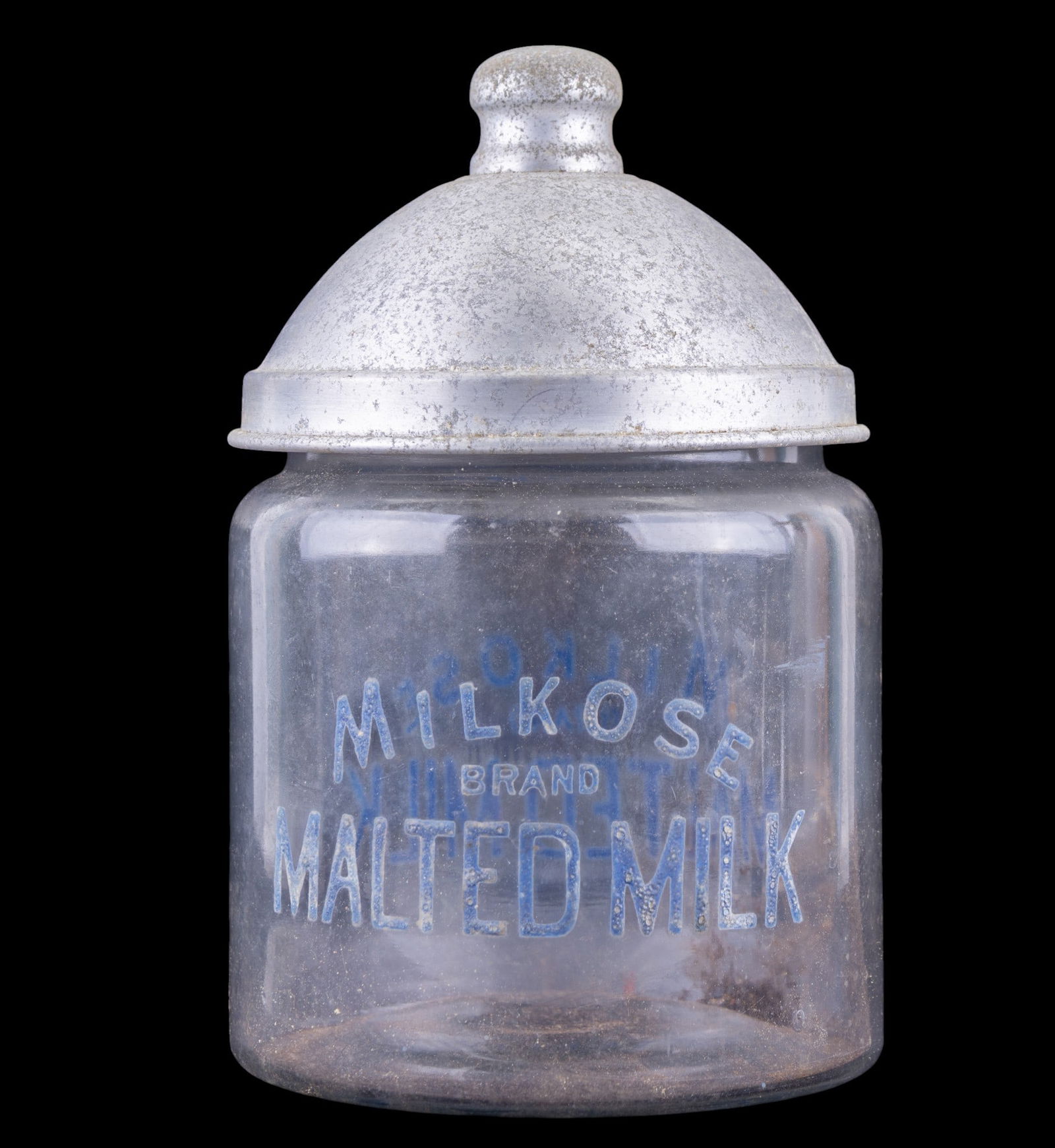 Vintage Milkose Malted Milk Display Jar: Vintage counter display jar for Milkose Brand Malted Milk, featuring a clear glass cylindrical jar with blue painted lettering reading "Milkose Brand Malted Milk." Measures approx. 9.5" H x 5.25"