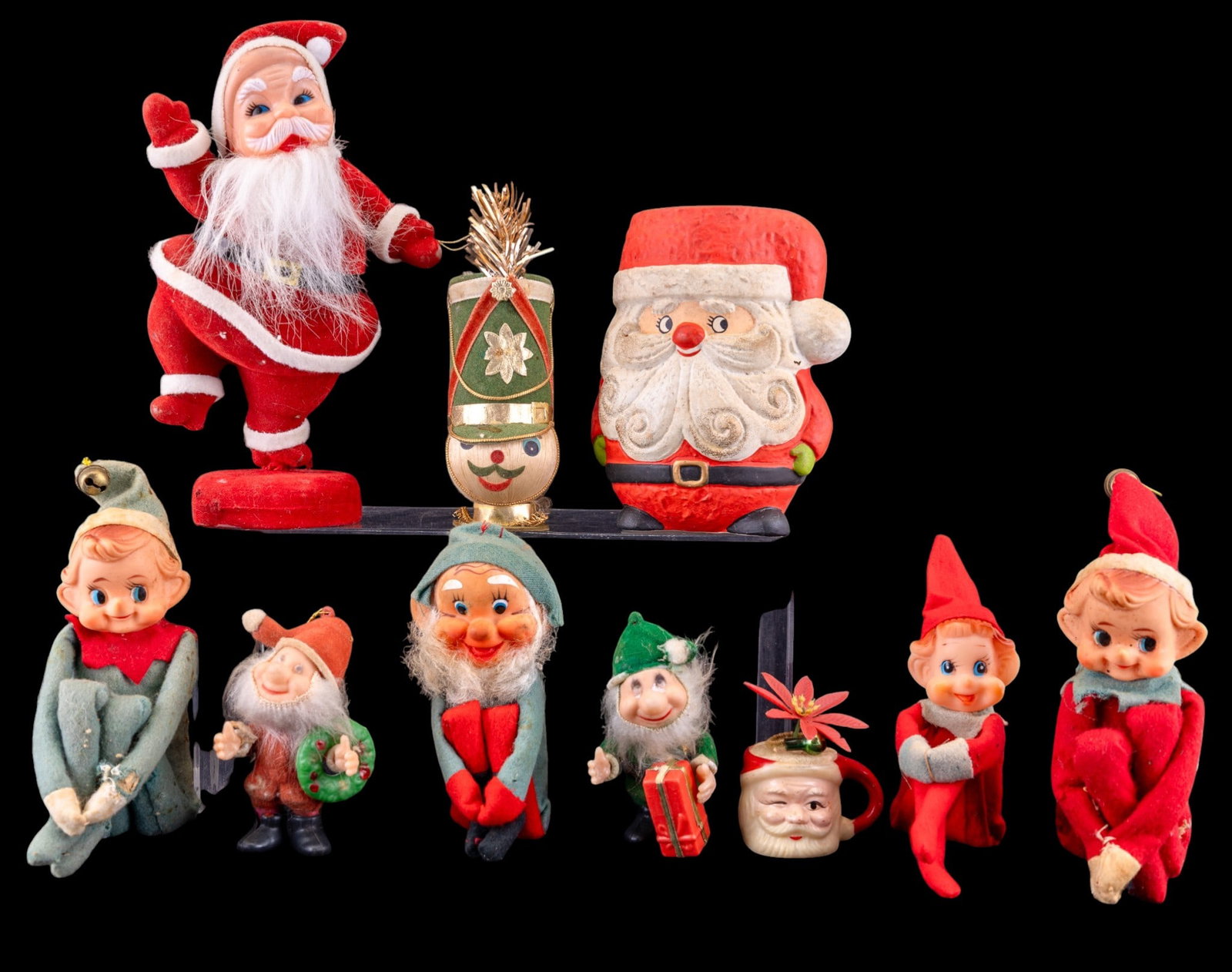 Vintage Knee Hugger Elves and Figurines: Vintage holiday-themed decorations including four knee hugger elves in fabric outfits, a Santa Claus wind-up toy or figurine, a cylindrical Santa container, a snowman with a drum, and additional small
