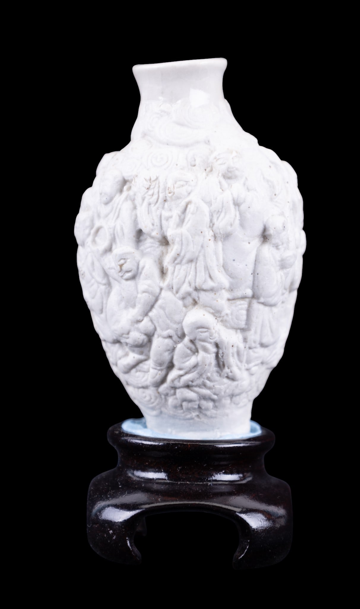 Chinese Porcelain Snuff Bottle: A Chinese white porcelain snuff bottle depicting a relief of multiple human figures, mounted to a wooden stand, total height is approx. 3.75" H.