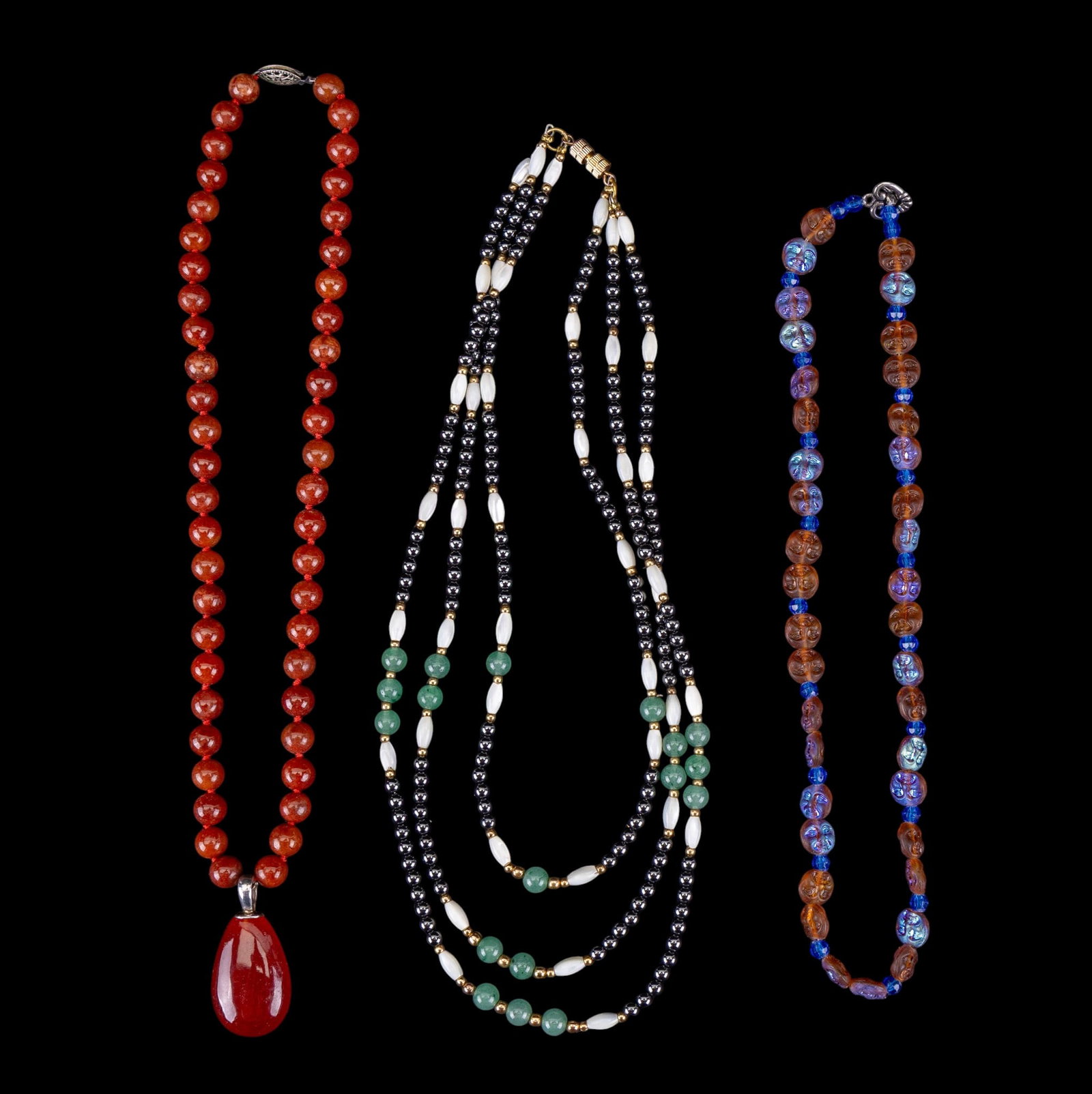 Fine Necklace Collection: A red jasper bead necklace with teardrop carnelian pendant with sterling bail and clasp, a hematite, green hardstone, and pearl necklace, and a moon-face lucite bead necklace, in the style of Kirks