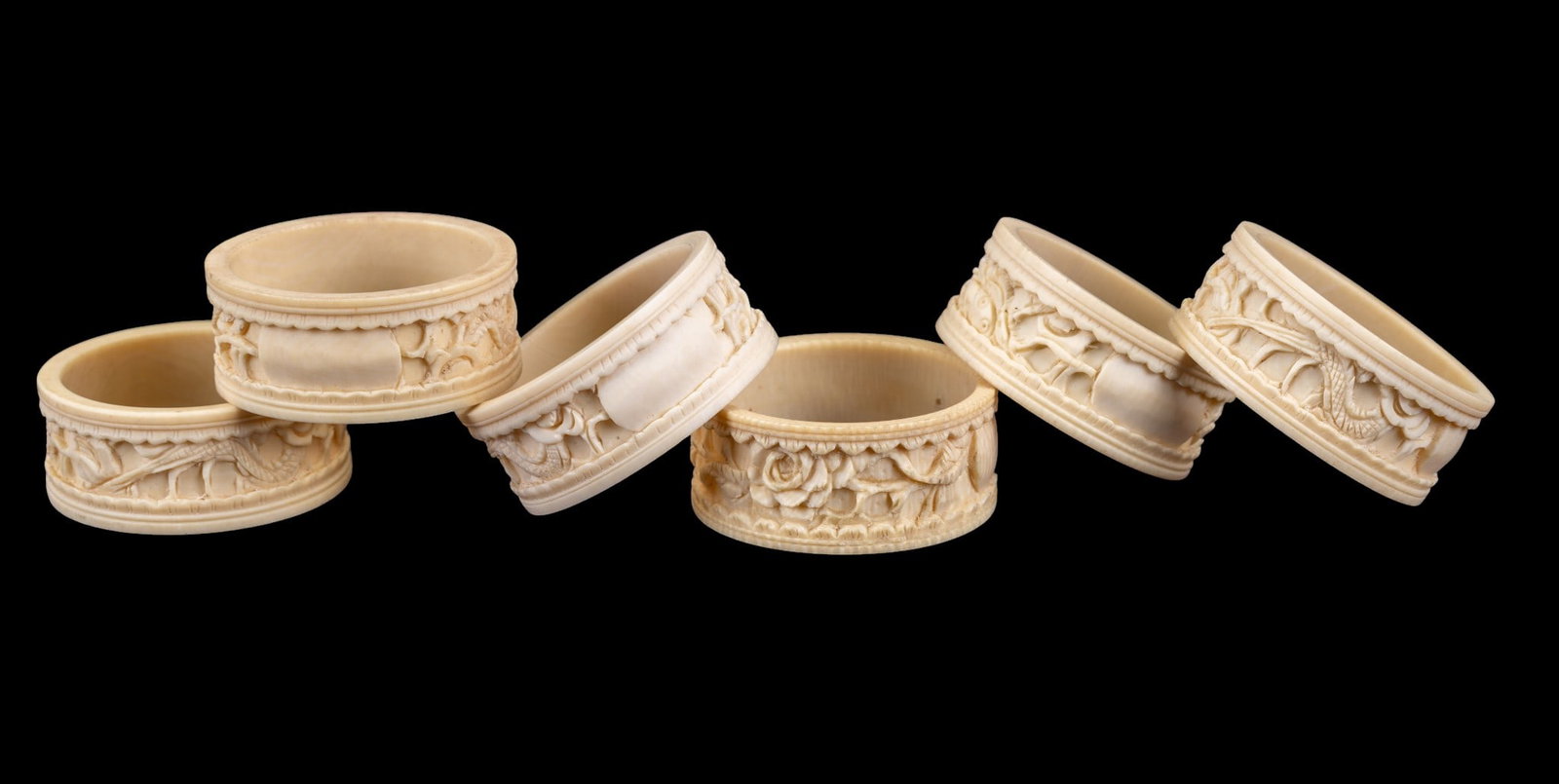 Carved Natural Material Figural Napkin Rings (6): Set of (6) carved natural material, each featuring continuous relief decoration with figural, floral, and landscape motifs. Each measures approx. 1.75" Diameter.