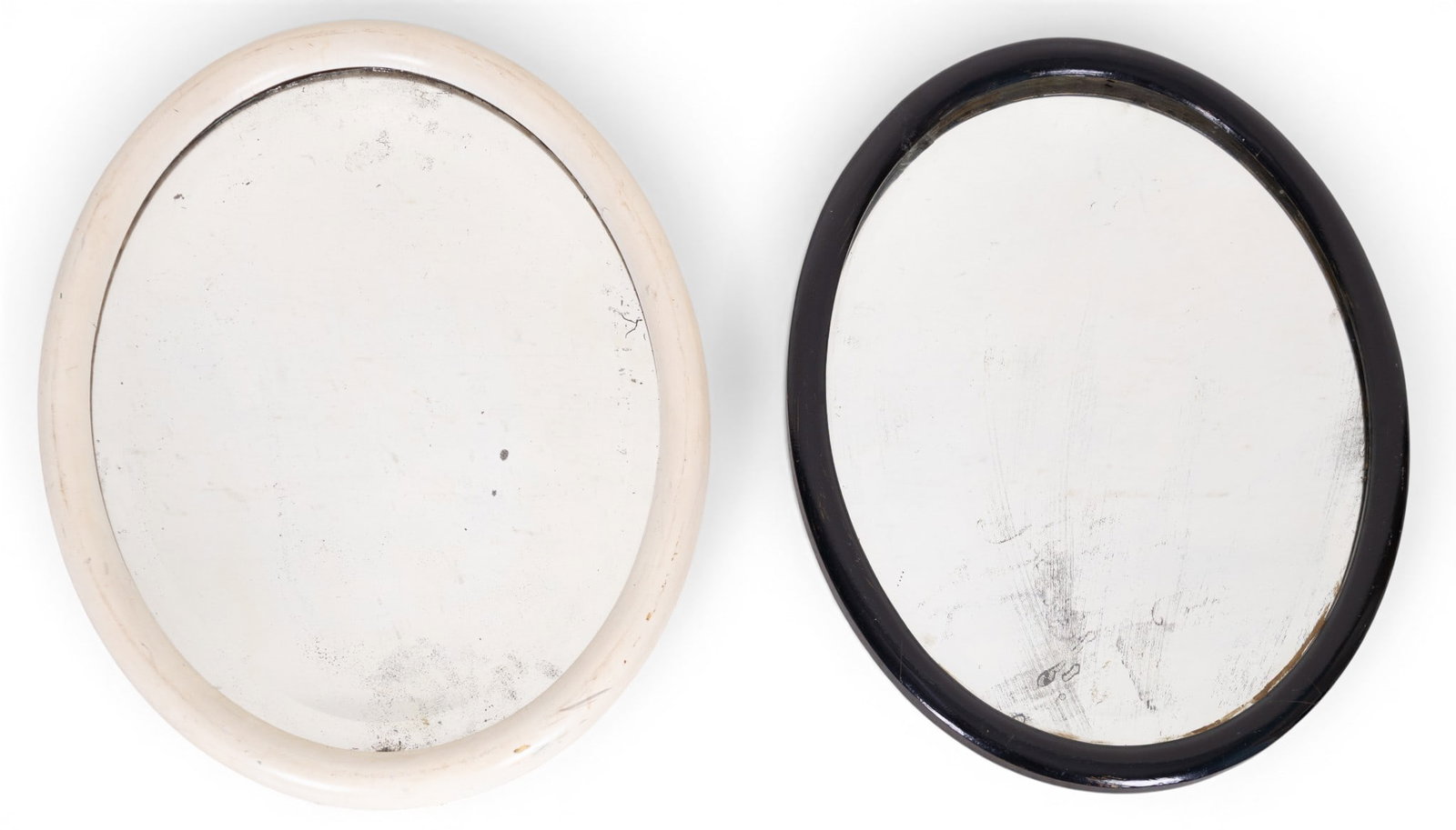 Antique Oval Beveled Mirrors (2): A collection of two antique oval beveled mirrors. One frame is painted off white (approx. 23" H x 18" W), while the other is painted black (approx. 21.5" H x 17" W).