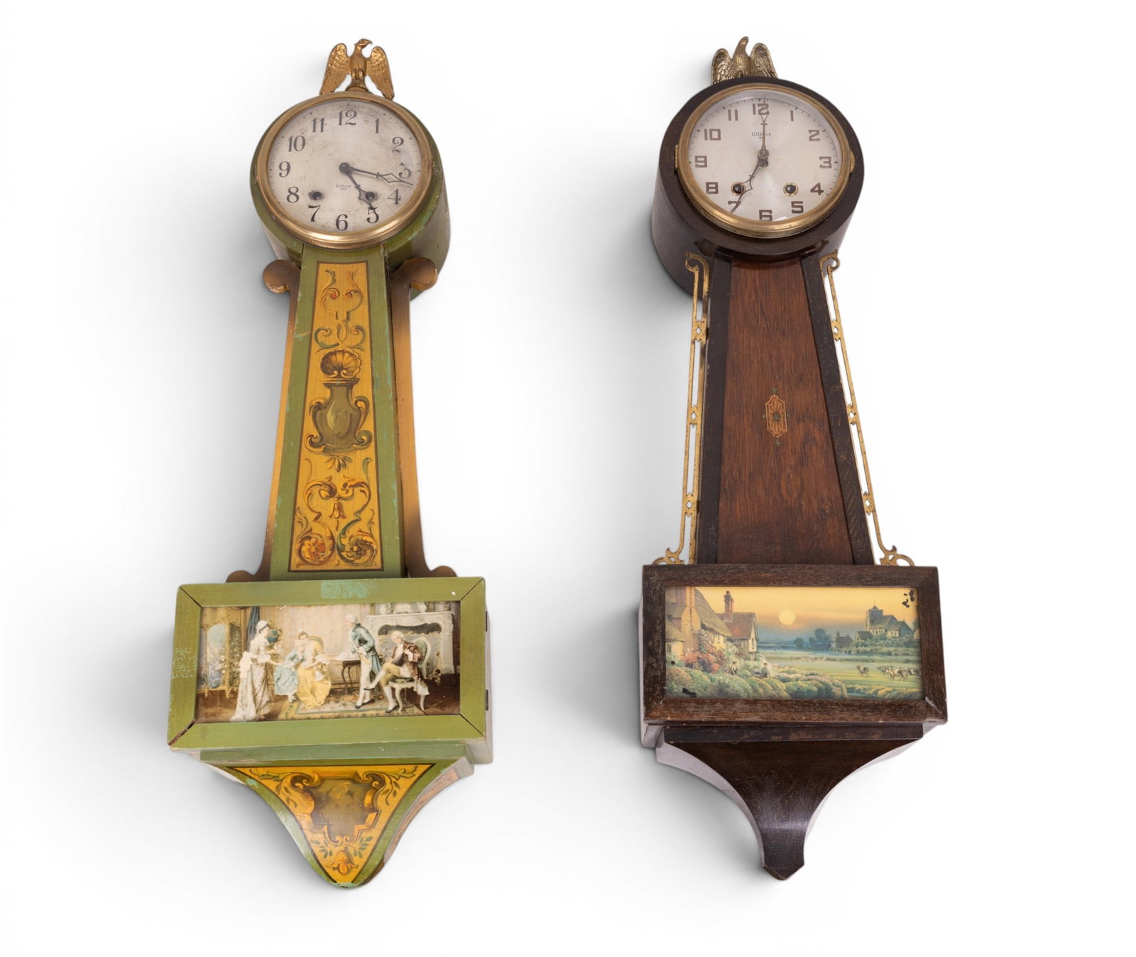 Pair of Gilbert USA 8-Day Banjo Clocks: Pair of William L. Gilbert Clock Company banjo clocks, each with spring-driven 8-day movements. One example in dark stained wood case with applied brass side mounts and lower glass panel depicting a s