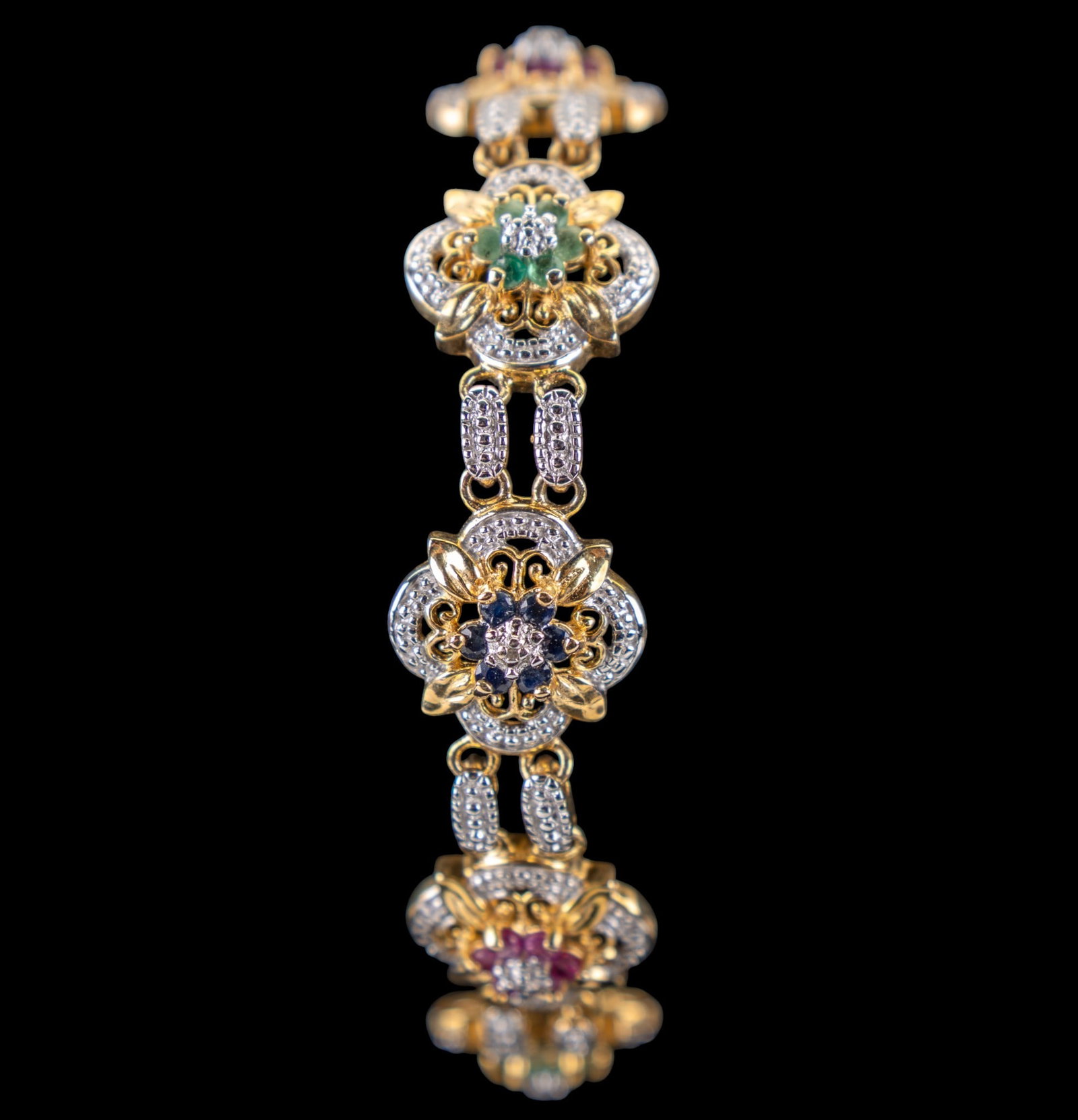 Floral Gemstone and Silver Bracelet: Sterling silver and vermeil bracelet set with sapphire, emerald and ruby stones; in a floral pattern
