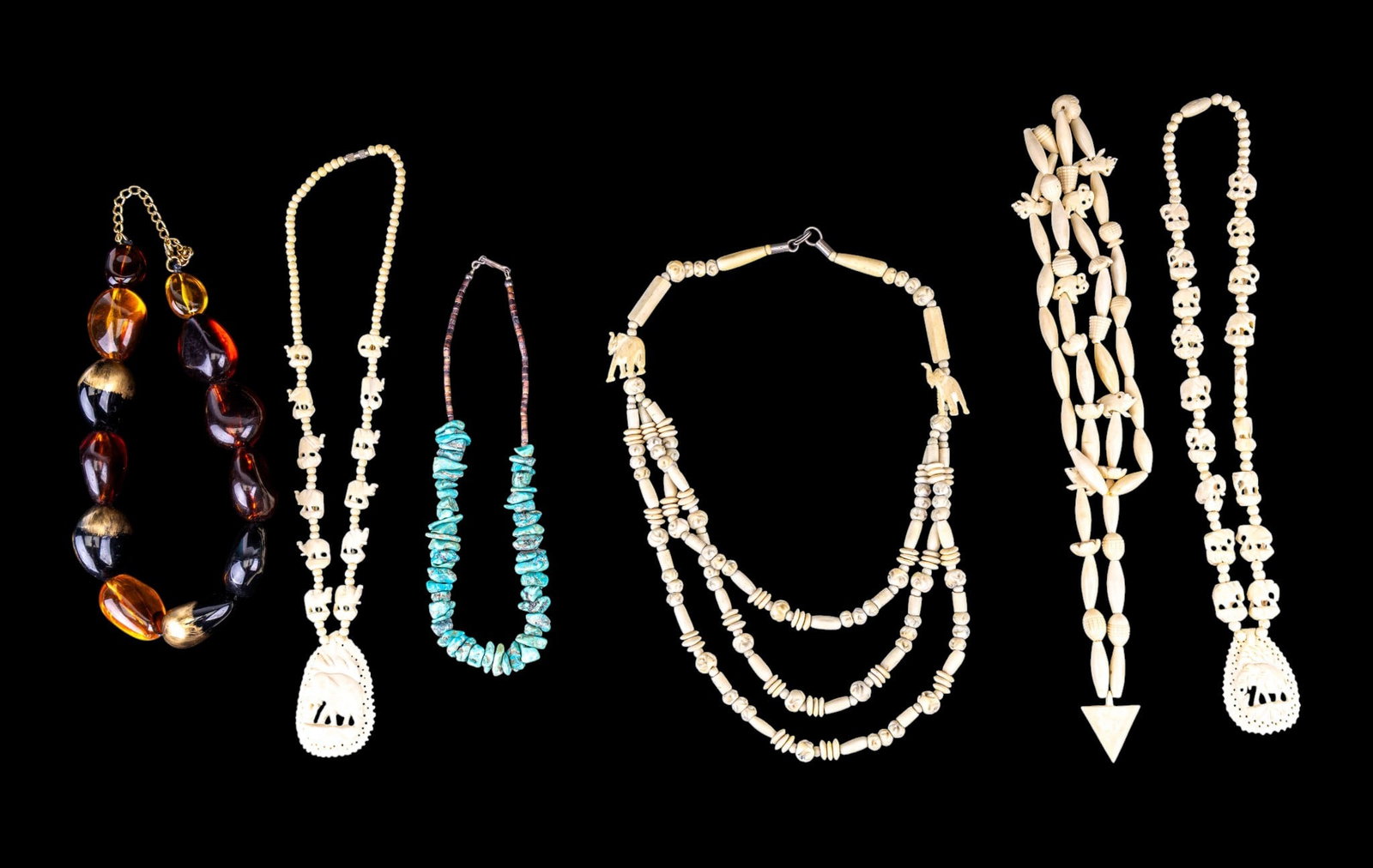 Carved Bead and Turquoise Necklaces: Four carved necklaces with elephant pendants and stations, a natural turquoise chunk necklace, and an oversized faux amber bead necklace. Longest measures approx. 18" on the drop.