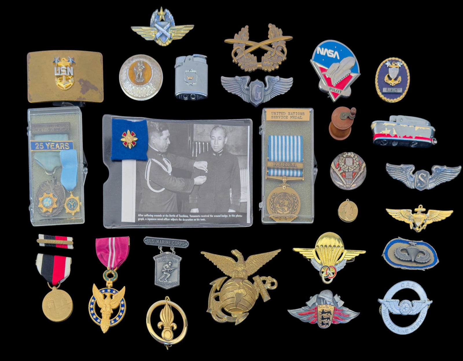 United States Military Insignia and More: A collection of United States Military insignia featuring an enamel NASA pilot pin, large USMC globe and anchor, USN belt buckle, United Nations Korea service medal, a post WWII Army of Occupation med