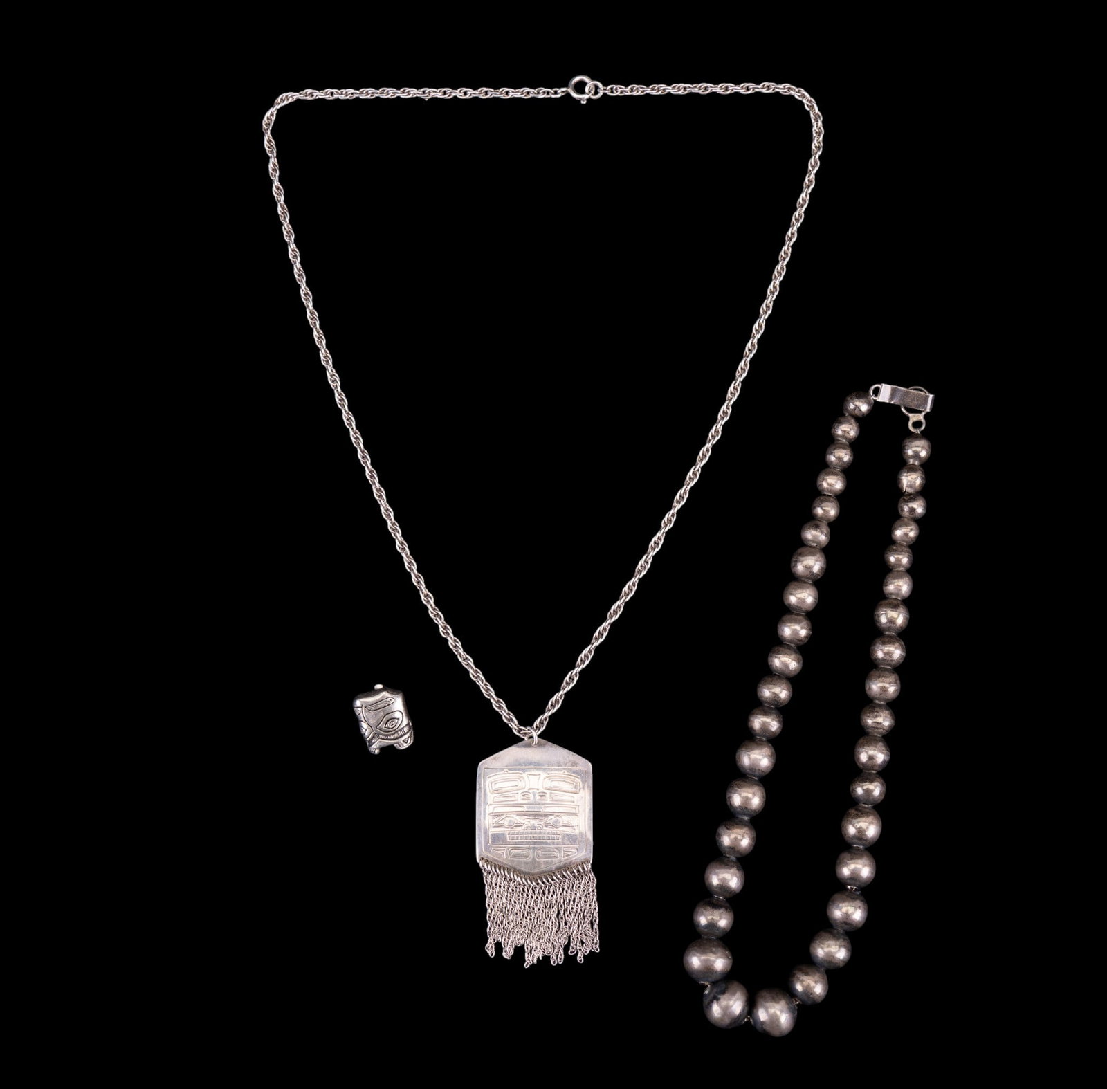 Sterling and Mexican Silver Necklaces: A Haida fringed sterling pendant on sterling chain, measures approx. 11" L on the drop, one clip on earring, and a graduated hollow bead necklace marked 'Silver Mexico'.