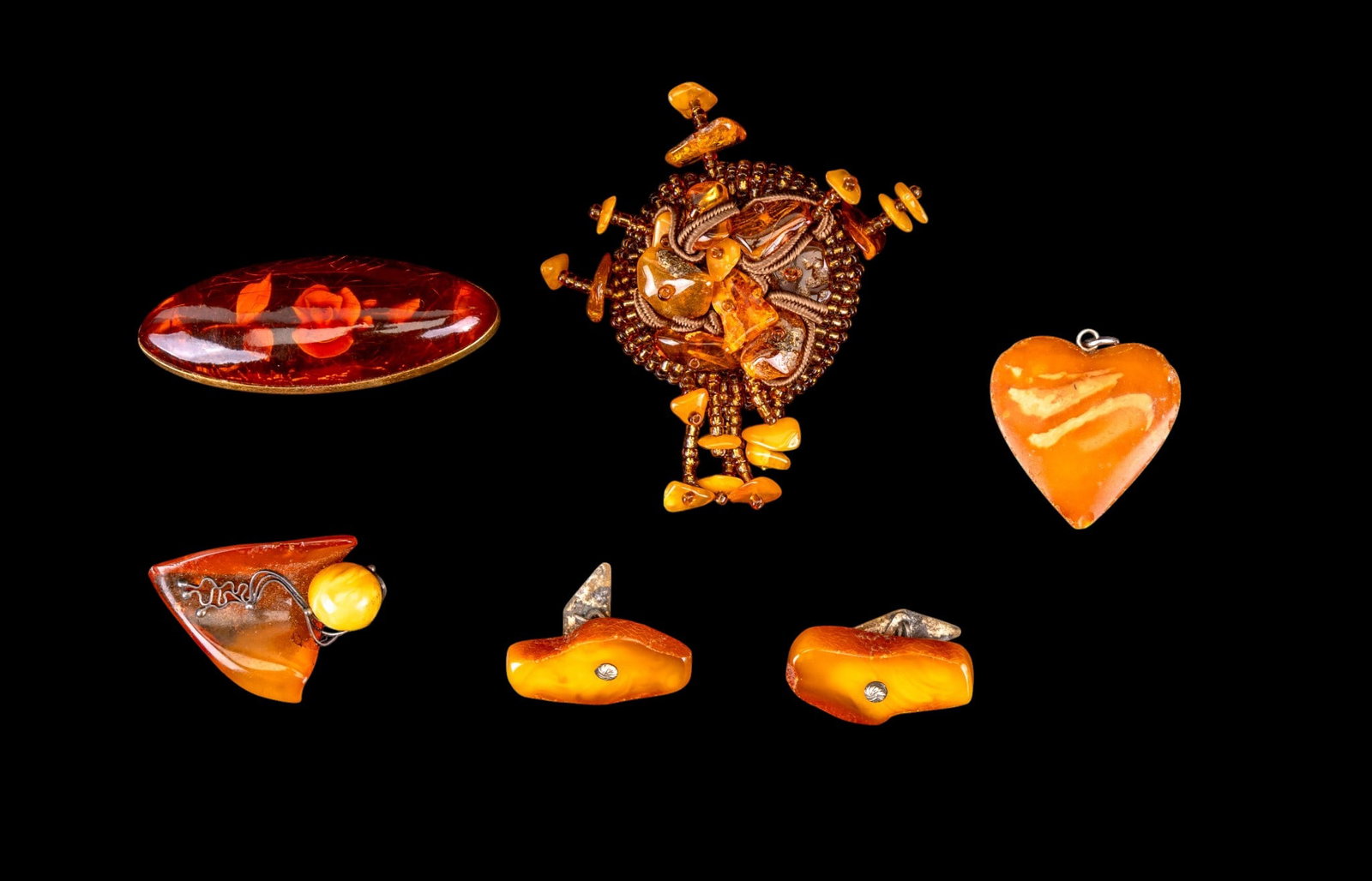 Early Amber Jewelry Grouping: A collection of early amber jewelry including a pair of butterscotch cufflinks, a heart shaped butterscotch pendant, an artisan crafted brooch featuring butterscotch and applejuice amber, an early bea
