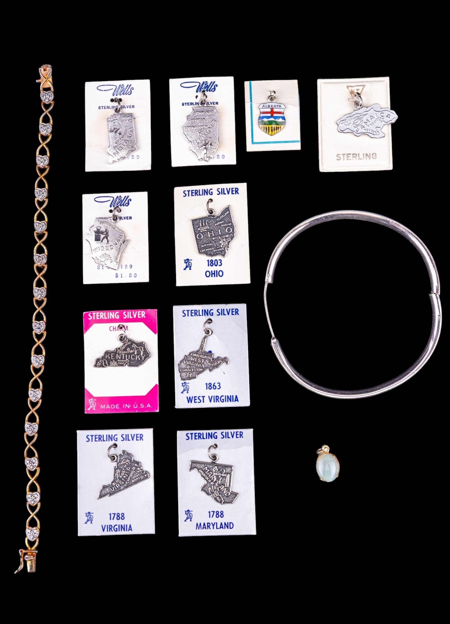 Sterling Silver Charms and Other Jewelry: A collection of sterling silver jewelry including charms depicting states, Jamaica, and Alberta, a hinged bangle bracelet, a heart tennis bracelet, and an opal oval cabochon and sterling pendant.