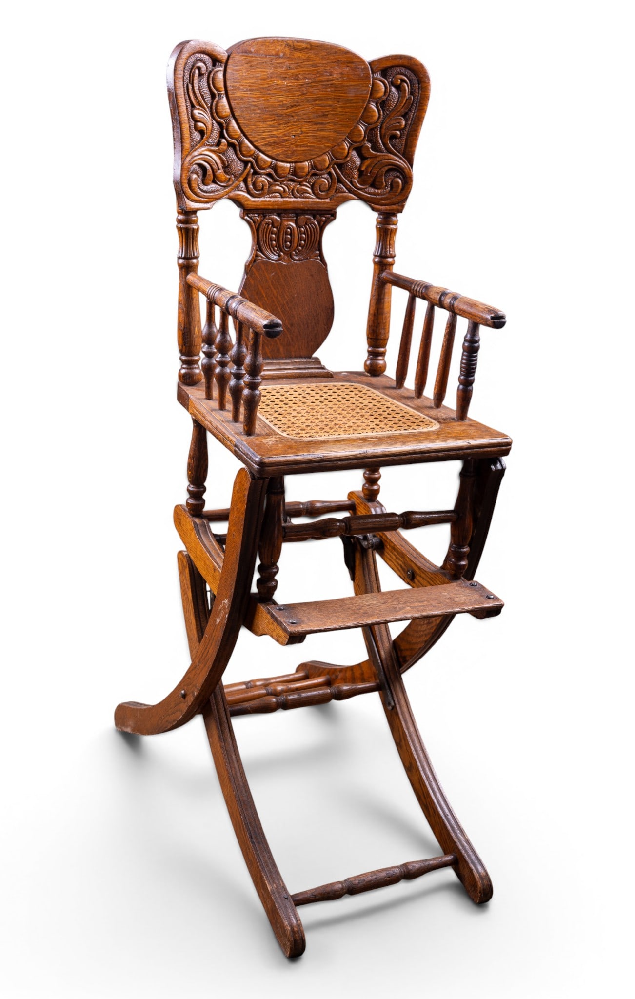 Pressed Oak Collapsible High Chair: Pressed oak child's high chair with carved crest, caned seat, turned spindle arms and legs. Measures approx. 13.5" W x 22.5" D x 40.75" H.