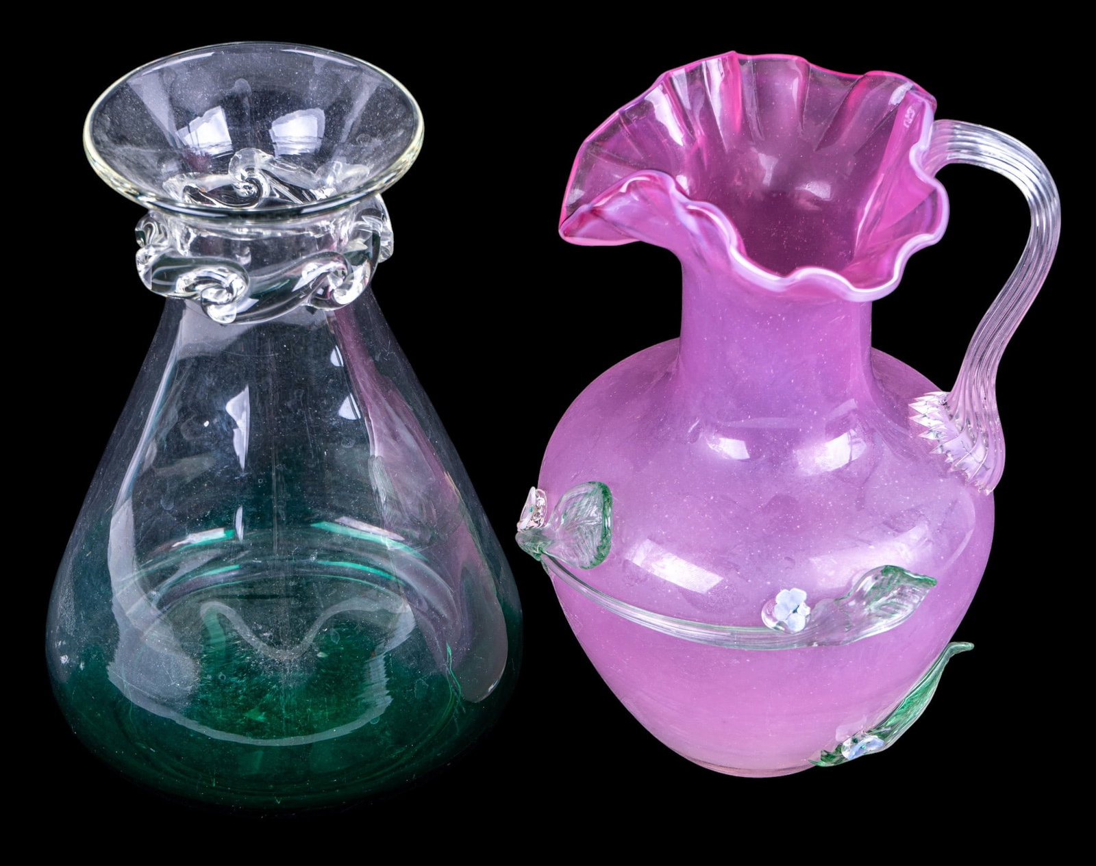 Pair of Hand Blown Art Glass Vases: Including a clear glass vase with emerald green tint to base and applied decoration to the neck, together with a pink satin art glass ewer having a clear applied handle, ruffled rim, and applied