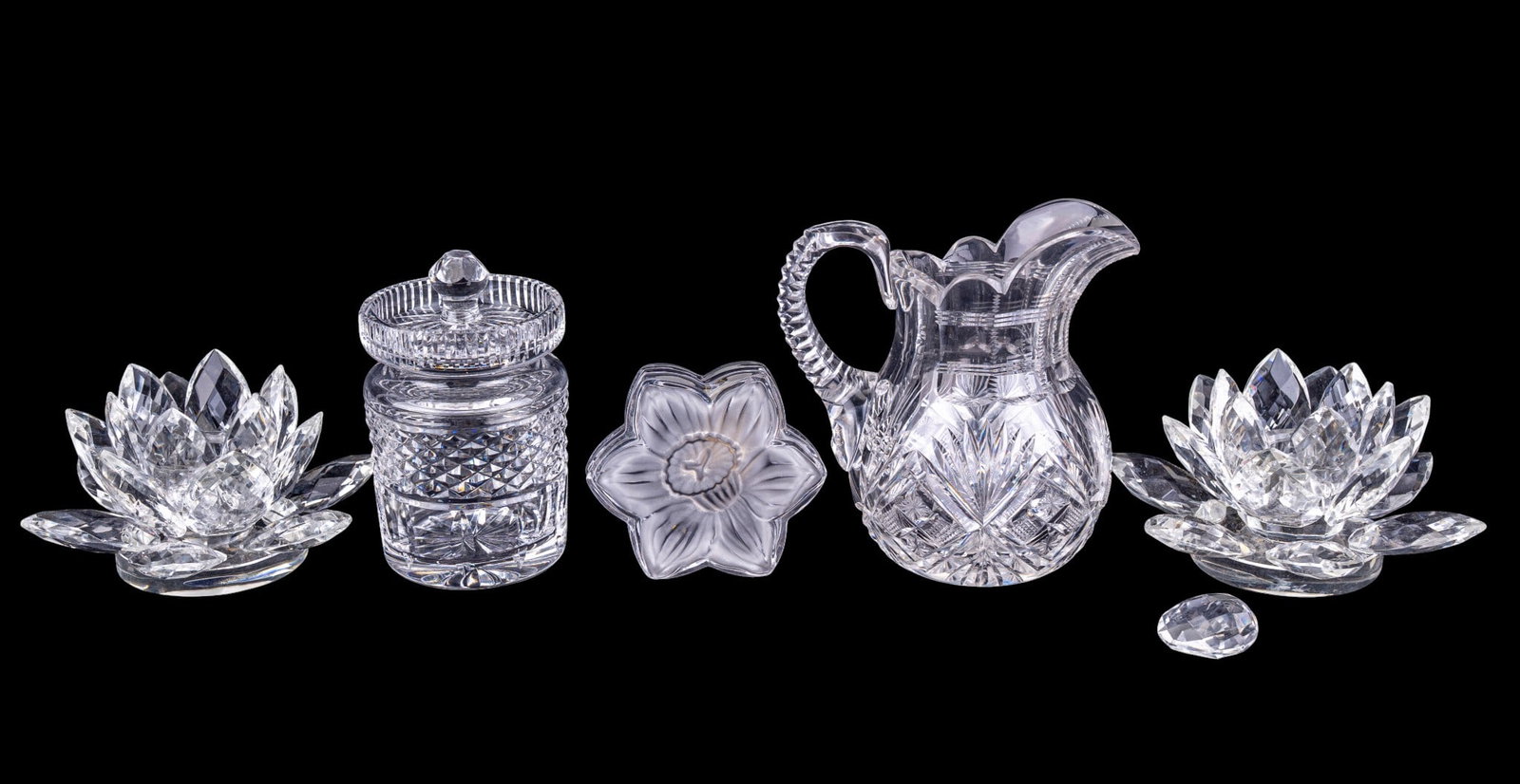 Crystal Table Items w/ Pitcher, More: Group comprising 2 Shannon Crystal lotus form candleholders, a flower-form crystal lidded trinket box, a cut crystal cylindrical lidded jar, and a cut crystal pitcher. One lotus candleholder has a det