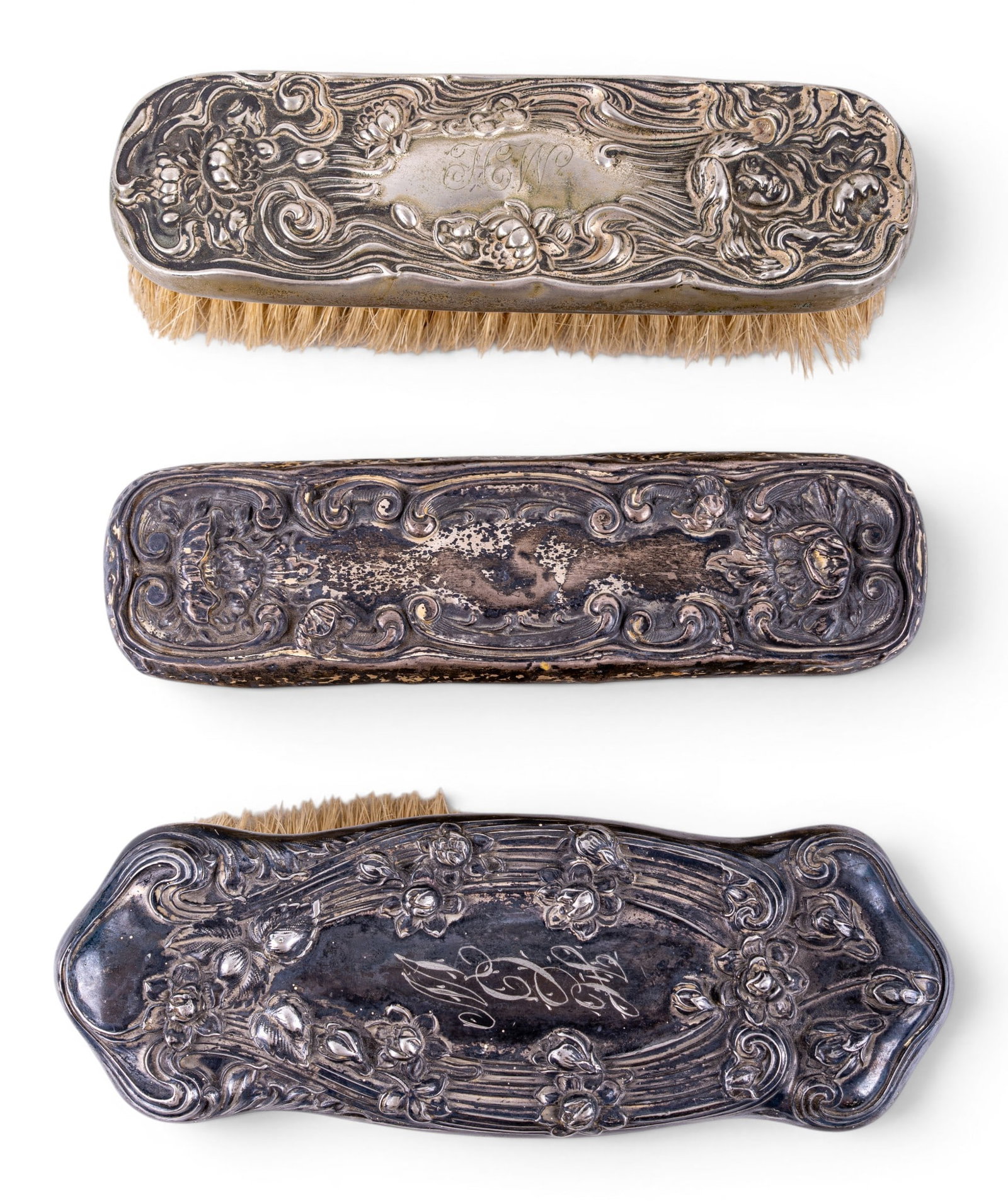 Art Nouveau Sterling Silver Mounted Brushes: Group of three dresser or clothes brushes with natural horsehair bristles and repousse decorated silver handles featuring scrolling foliate and floral Art Nouveau motifs. 2 Examples are marked Sterlin