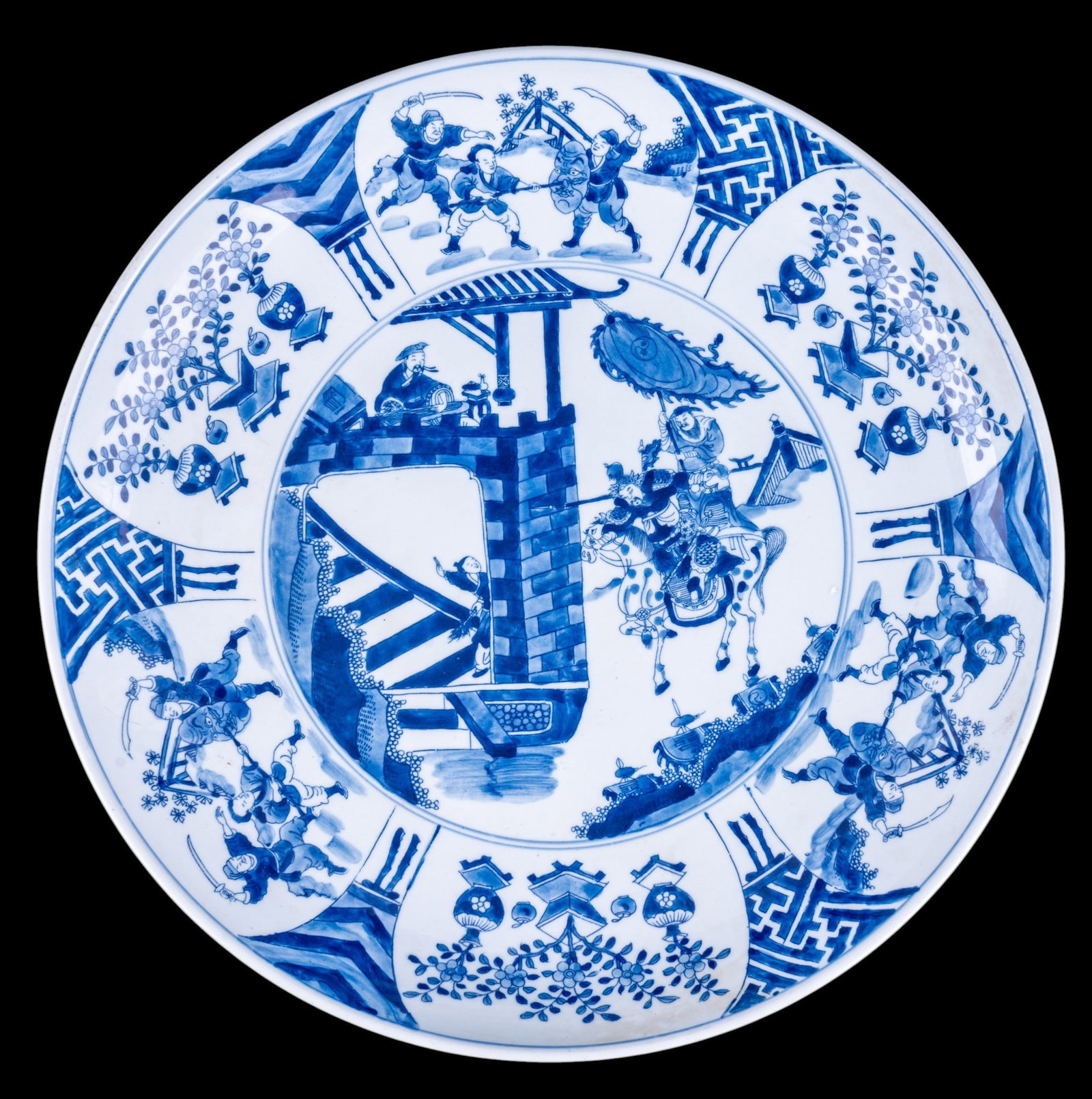 Chinese Blue and White Figural Charger: Large Chinese hand painted blue and white porcelain charger depicting a mounted military figure with attendants, surrounded by alternating panels of warriors, floral arrangements, and geometric decora