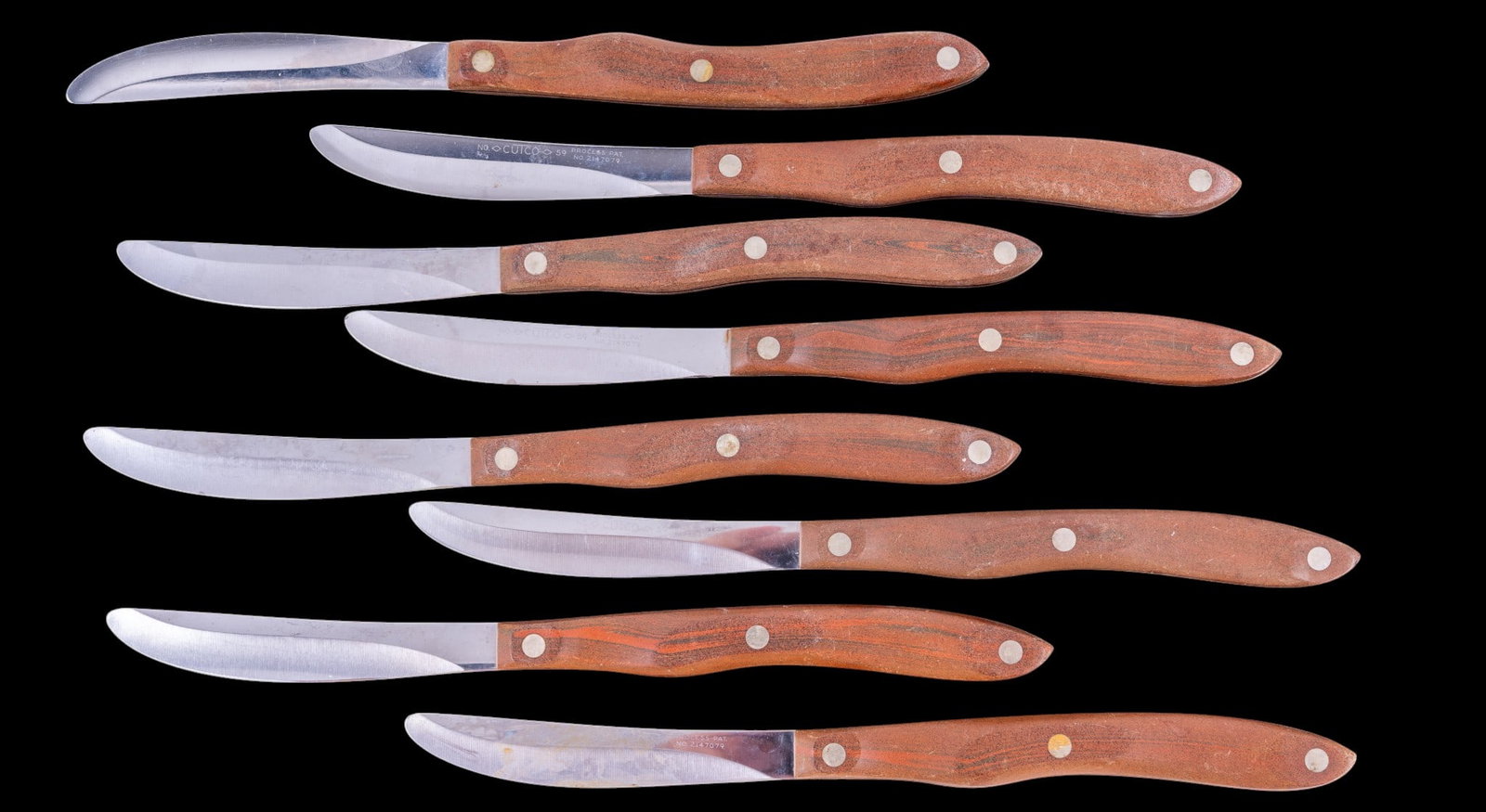 Set of 8 Cutco Table Knives: Set of eight Cutco stainless steel table or steak knives with shaped wood handles and brass-tone rivets. Blades marked Cutco.