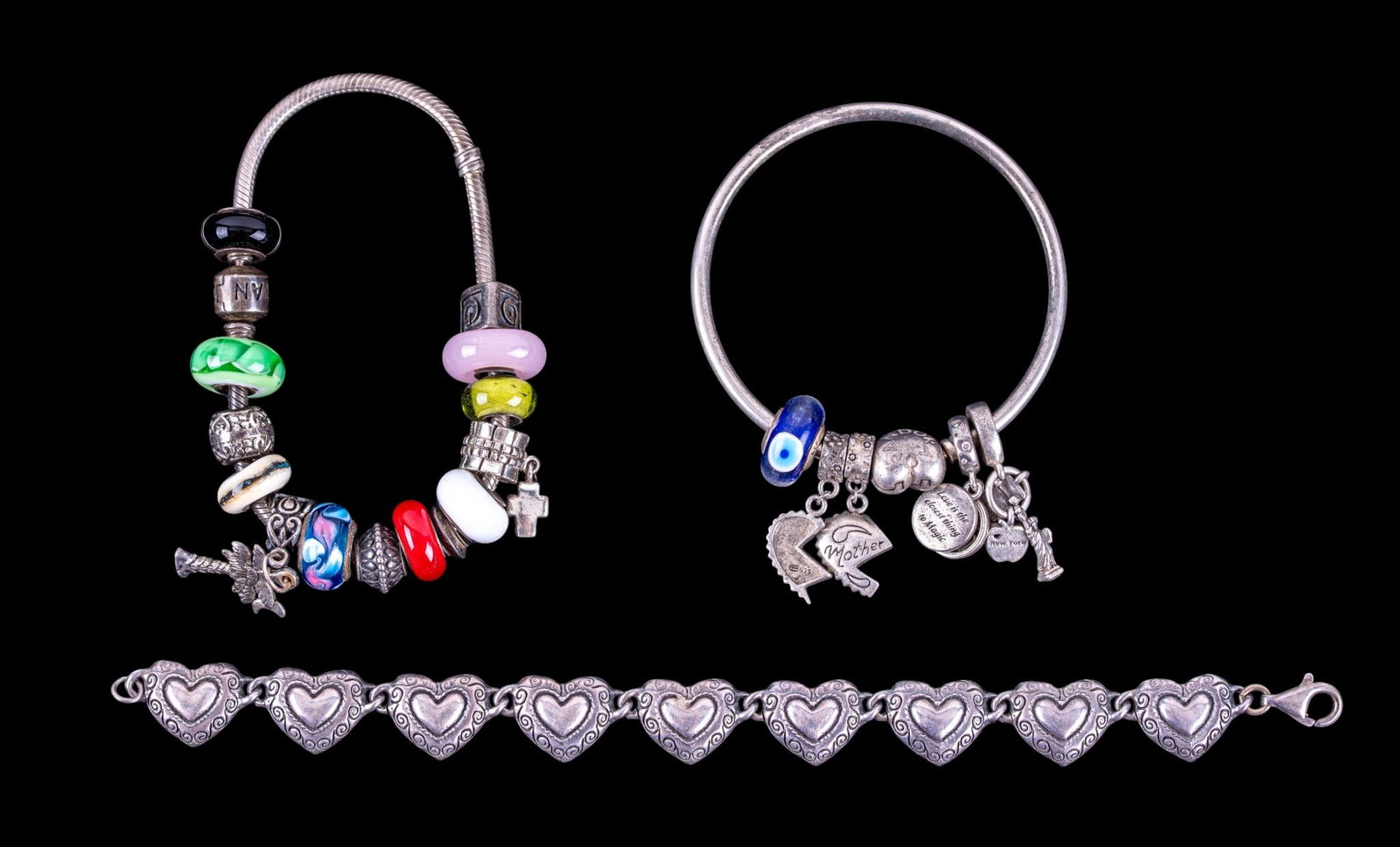 Brighton and Pandora Sterling Silver Bracelets: A Brighton sterling silver heart shaped panel bracelet, and two Pandora bracelets featuring 18 charms, not all marked. Total weight is approx. 3.15oz.